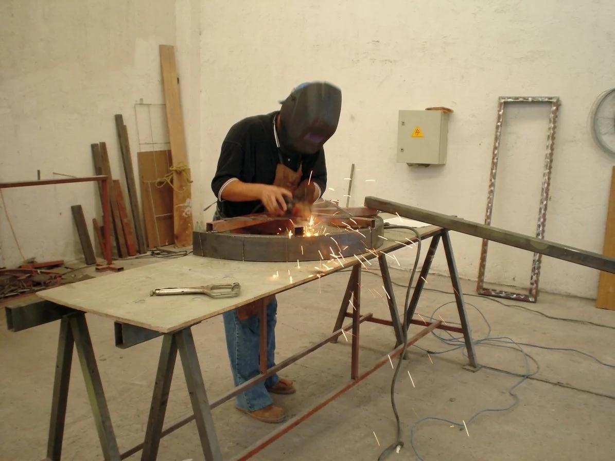 A person welding metal pieces near a workbench in a workshop.