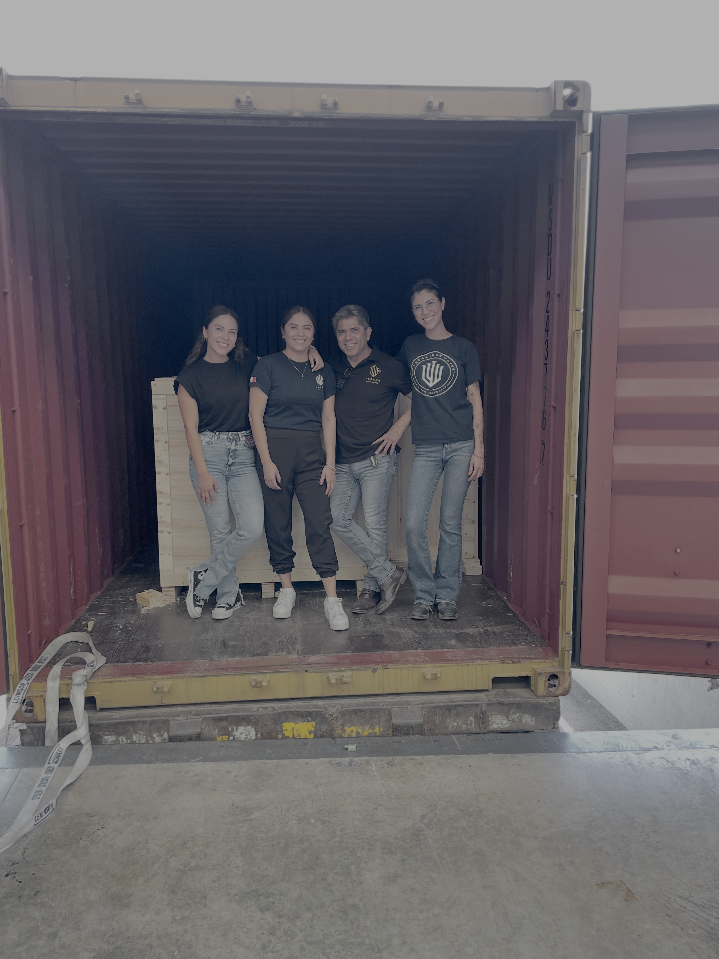 Four people standing inside a shipping container, smiling and posing for the photo. They are dressed casually, with two women on the ends and two men in the middle.
