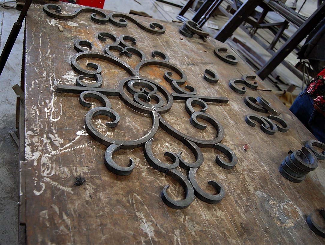 Iron decorative wall piece with intricate scrollwork on a wooden workbench in a workshop.