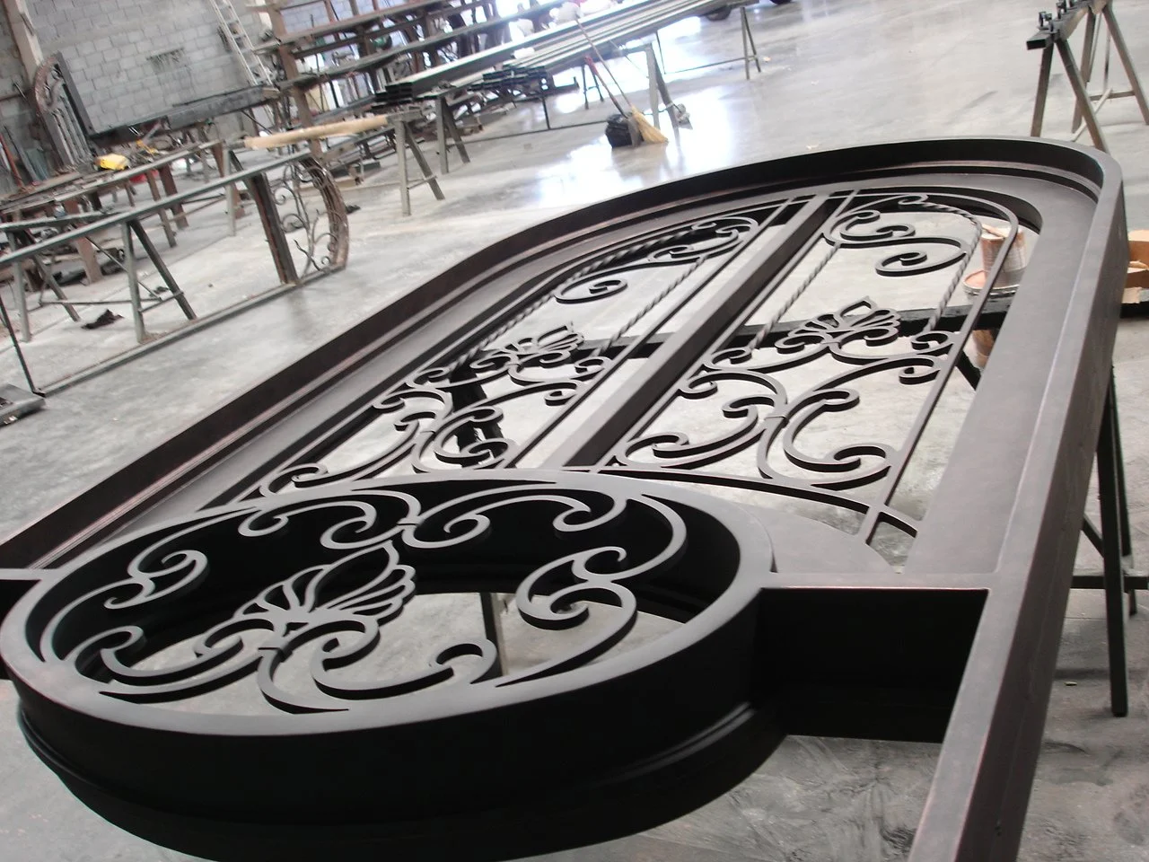 A metal decorative sign frame with intricate scrollwork design, resting on a worktable in a workshop.