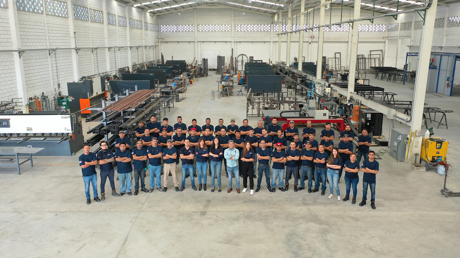Group of workers standing in a line inside a large industrial warehouse filled with manufacturing equipment and machinery.