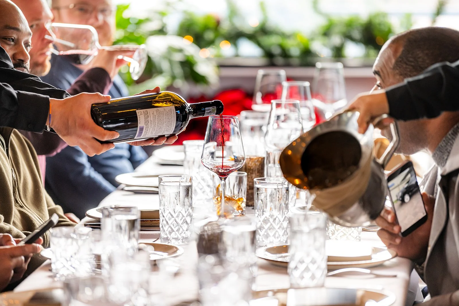 People seated at a dining table having wine, as servers pour and serve wine at a formal gathering.