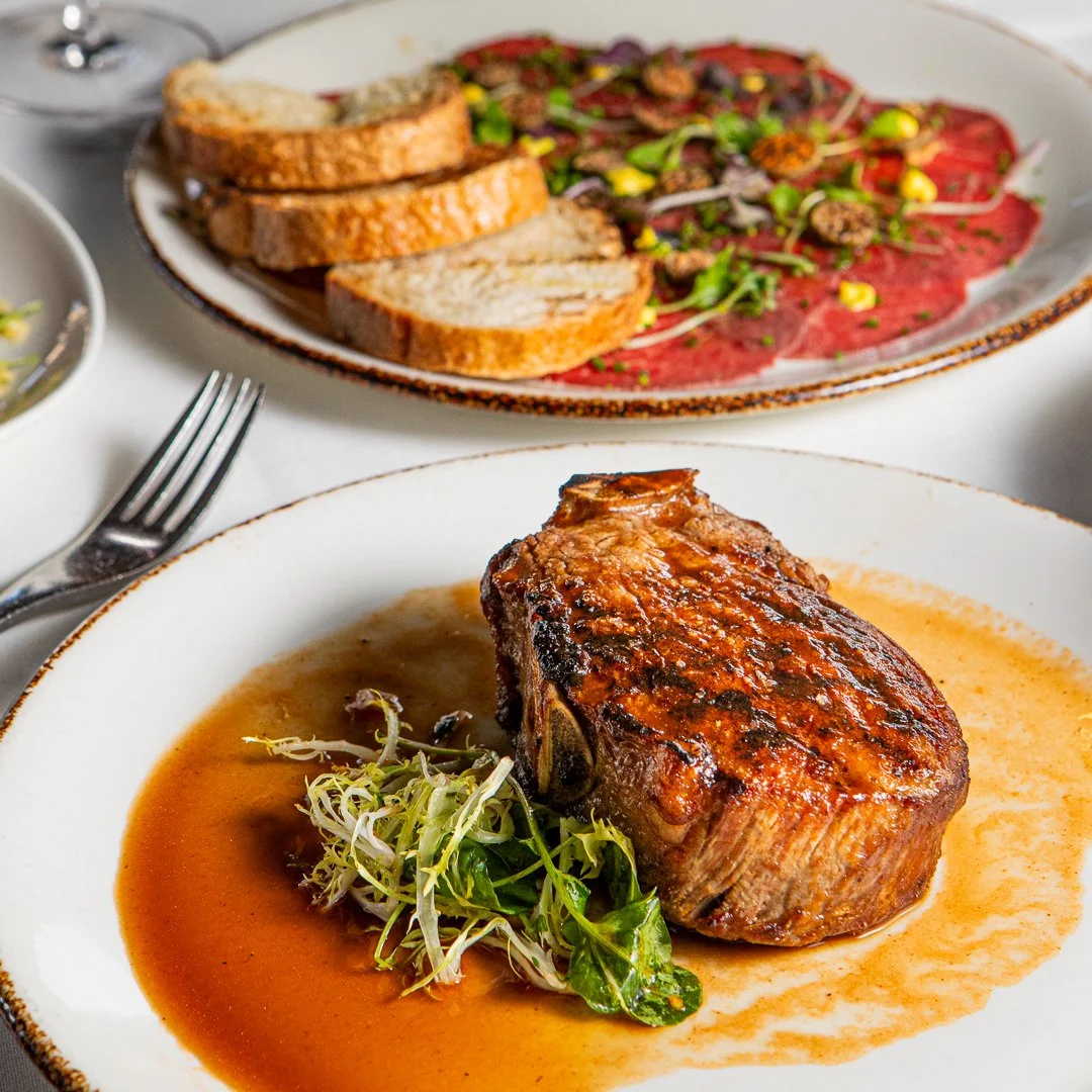 A plated dinner featuring a cooked steak with sauce and greens, served with a side of sliced toasted bread and a salad with mixed greens and vegetables.