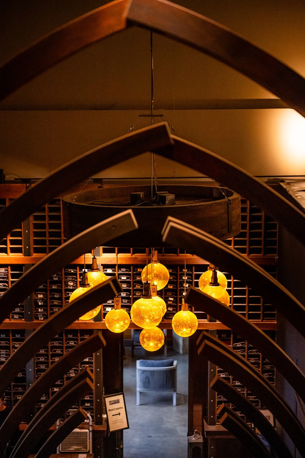 Hanging yellow globe light fixtures in a dimly lit wine cellar or tasting room with wine storage racks in the background.