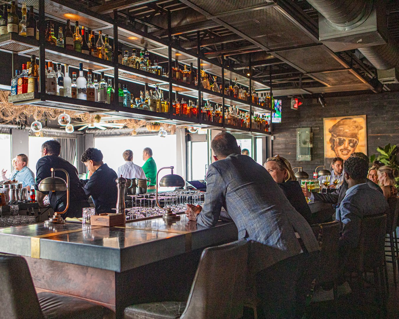 People sitting at a bar inside a restaurant or bar with bottles of alcohol displayed on shelves above the bar counter.