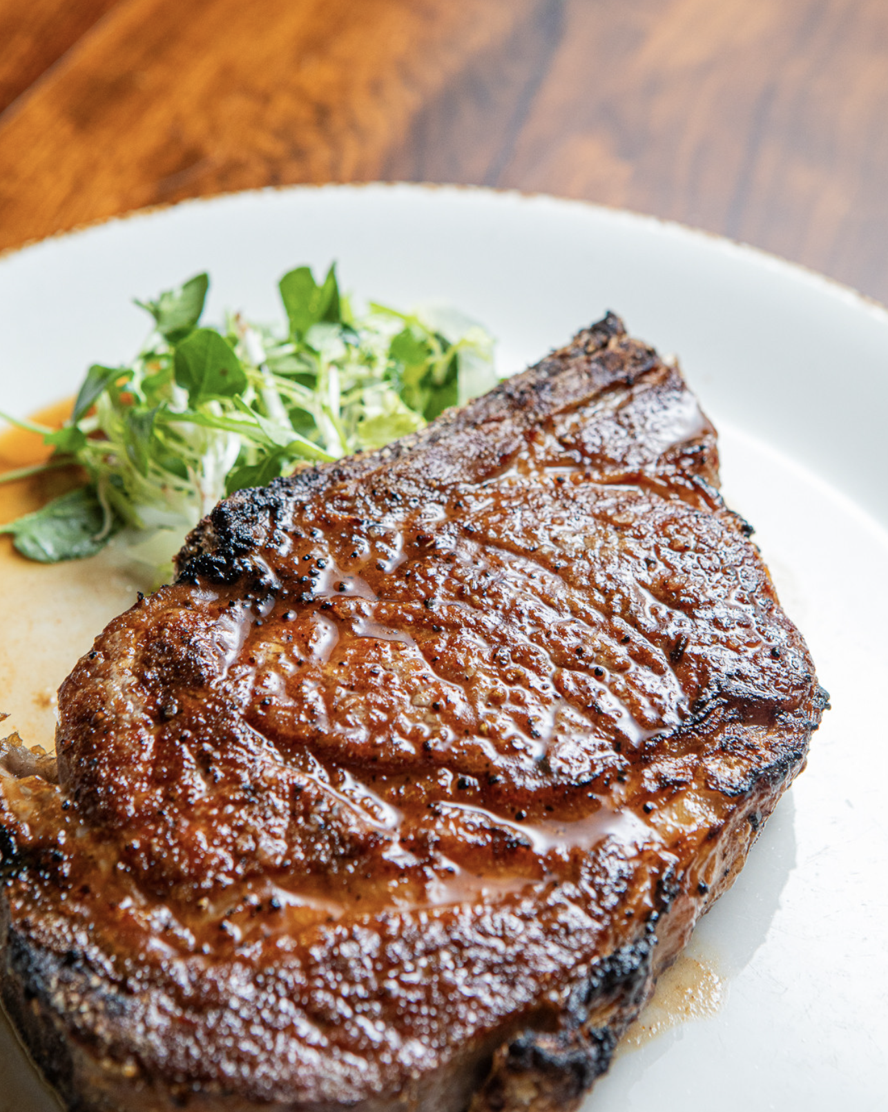 A cooked steak with grill marks and sauce on top, served with a side of leafy salad greens on a white plate.