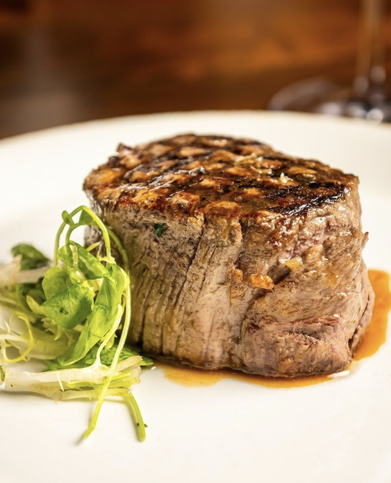 Seared steak with a side of mixed greens on a white plate.
