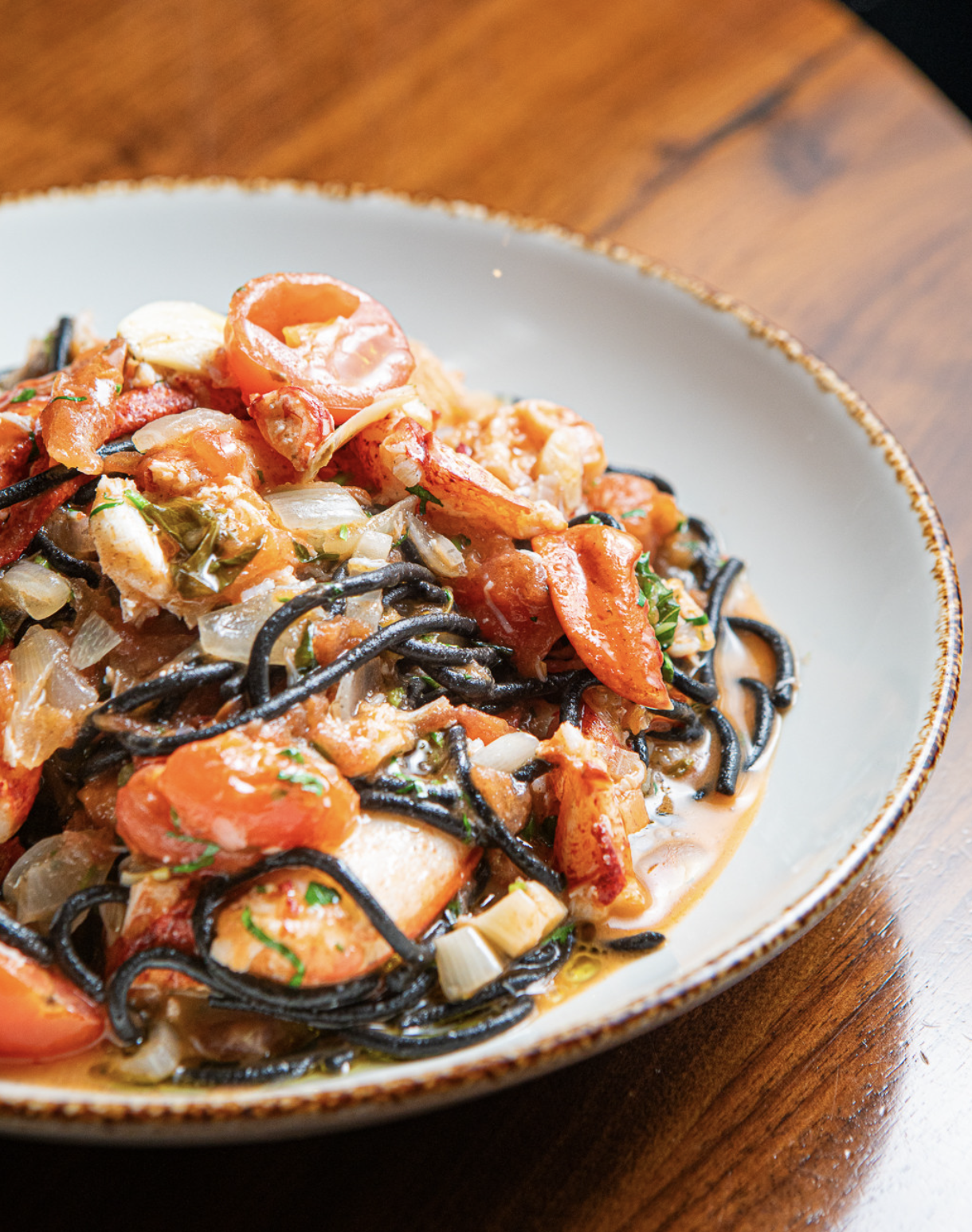 Plate of black squid ink pasta with tomatoes, chicken, onions, and herbs