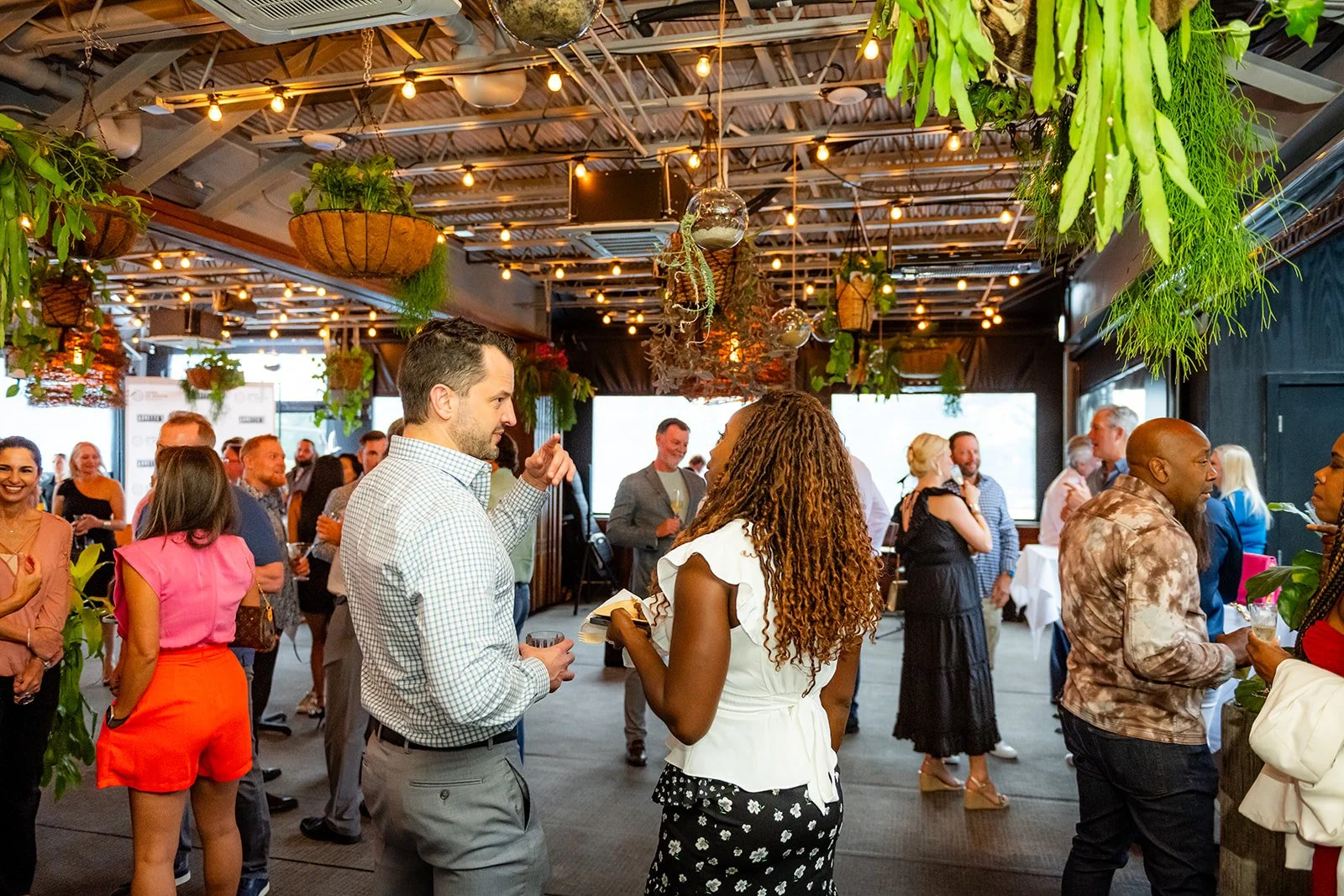 People socializing at a lively indoor event with hanging plants and warm lighting.