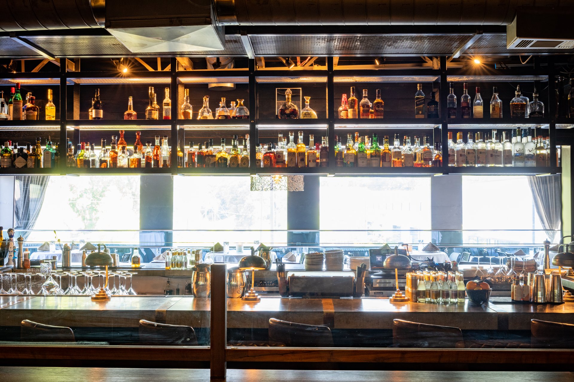 Bar with bottles of liquor on shelves, bar counter with glasses and bar tools, bright window in the background, interior of a restaurant or bar