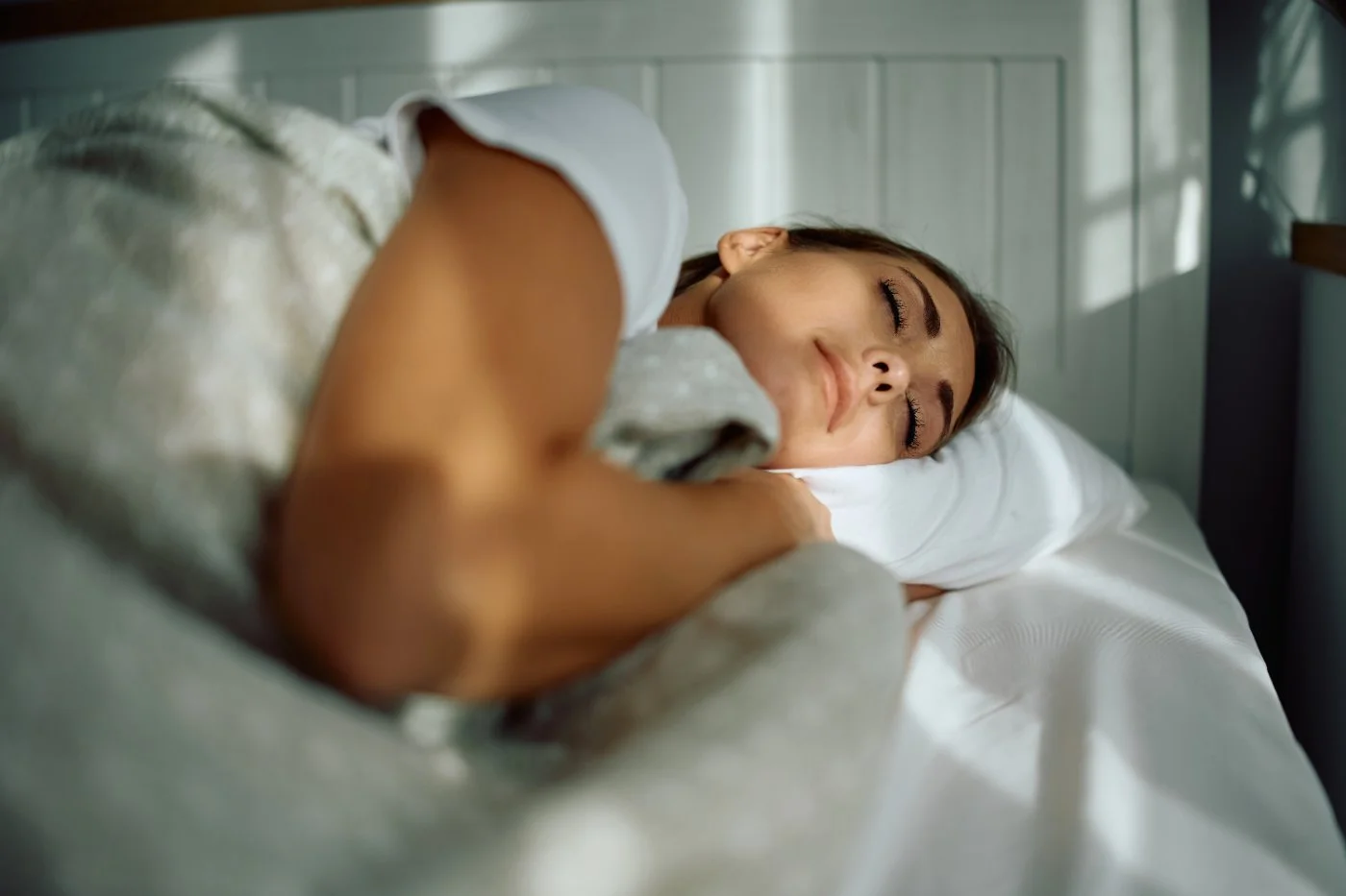 Orin App woman sleeping on a bed, hugging a pillow, in a cozy room with soft lighting.