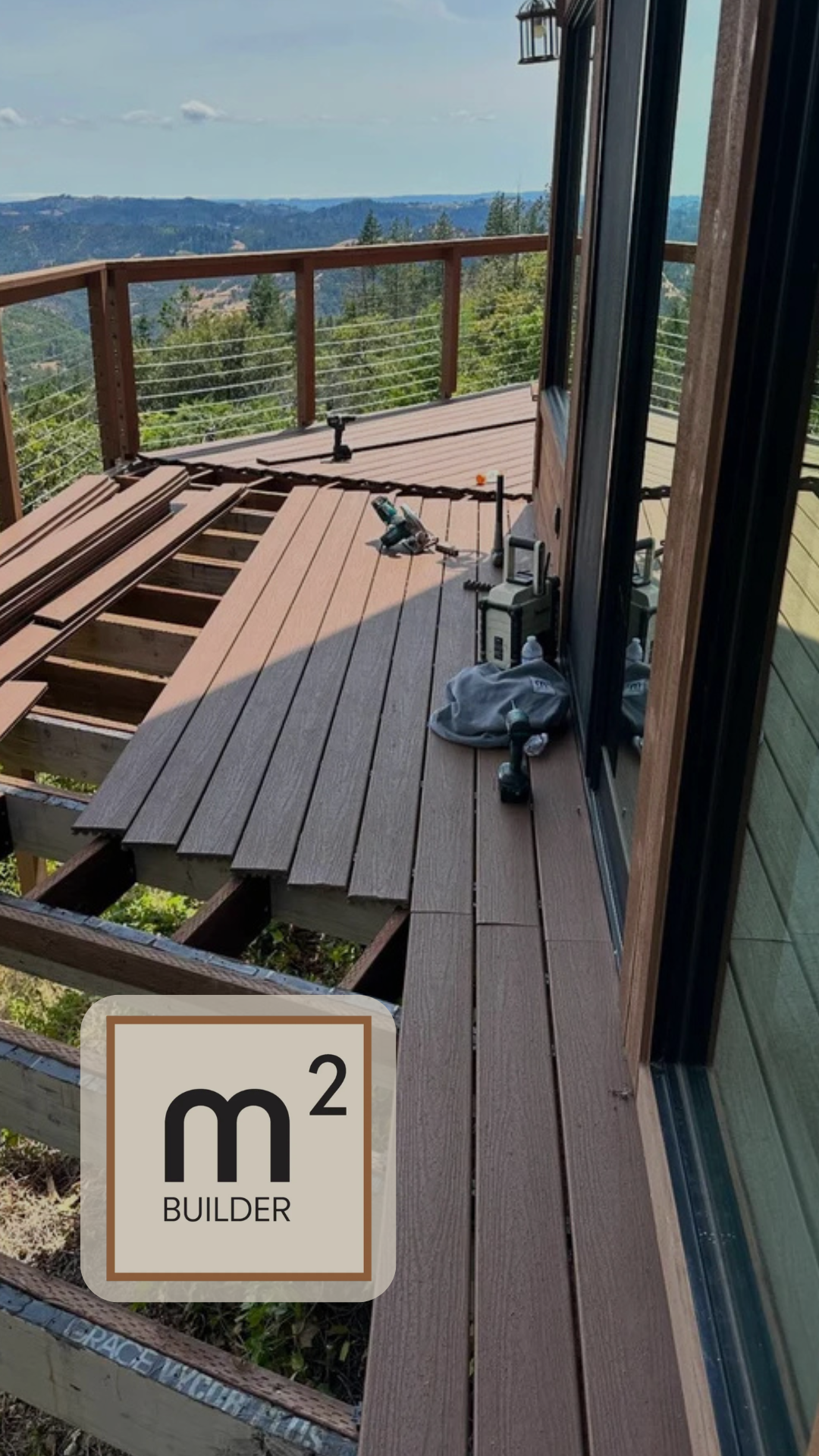 A balcony under construction with wooden planks partially installed, construction tools and materials scattered on the floor, and a scenic view of forested hills in the background.