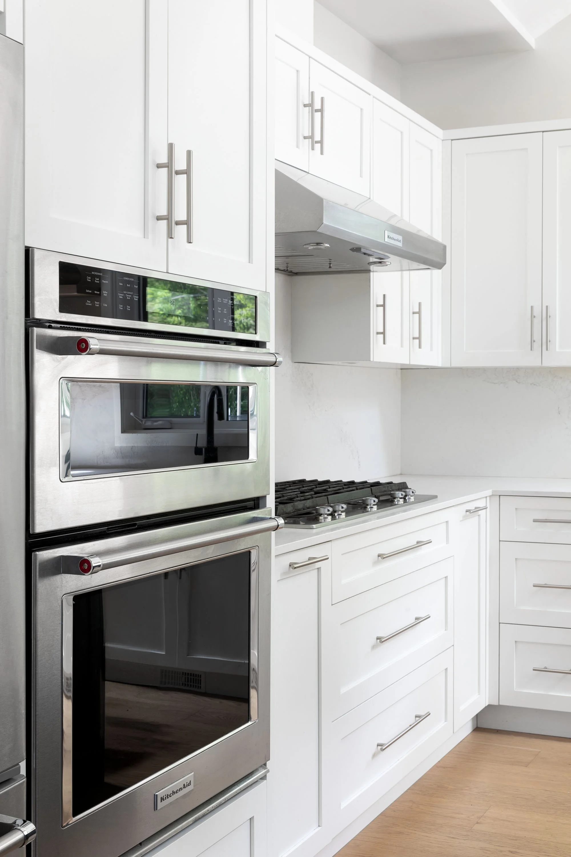 Modern kitchen with white cabinets, stainless steel oven, stove, and range hood, light wood flooring.