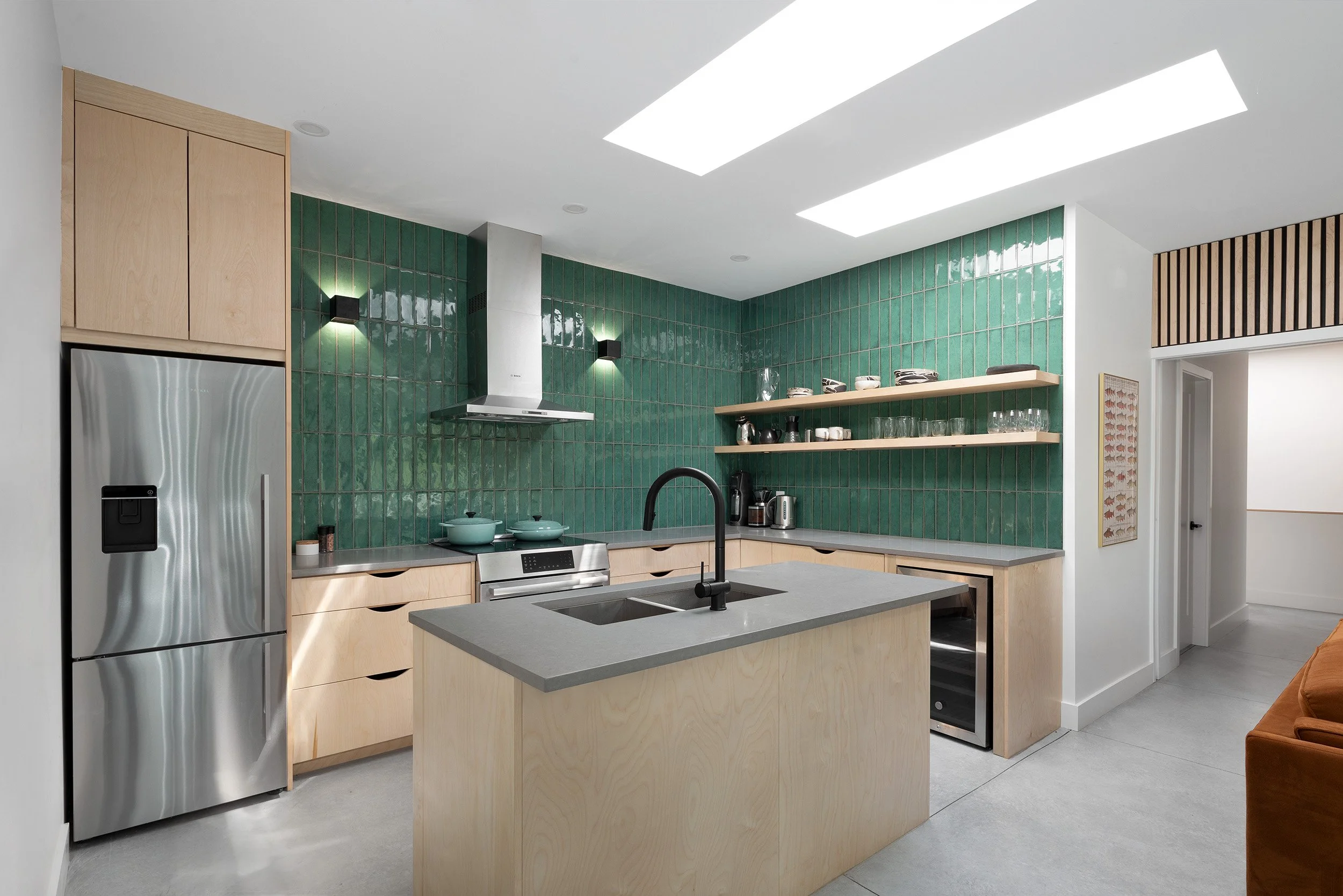 Modern kitchen with green tiled backsplash, wooden cabinetry, stainless steel appliances, and a kitchen island with a black faucet.