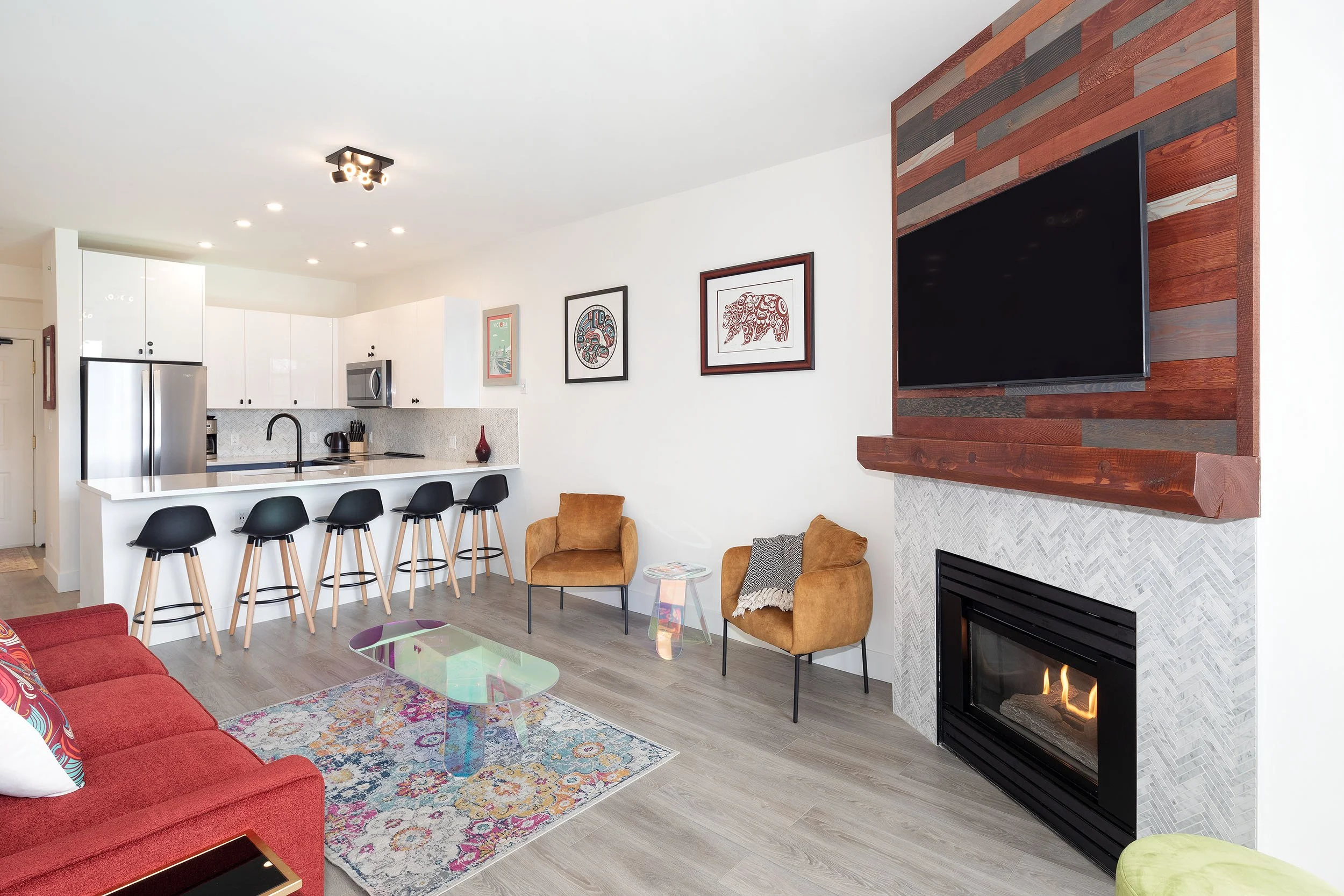 Open-concept living room and kitchen with colorful decor, fireplace, wall art, and barstools at kitchen counter.