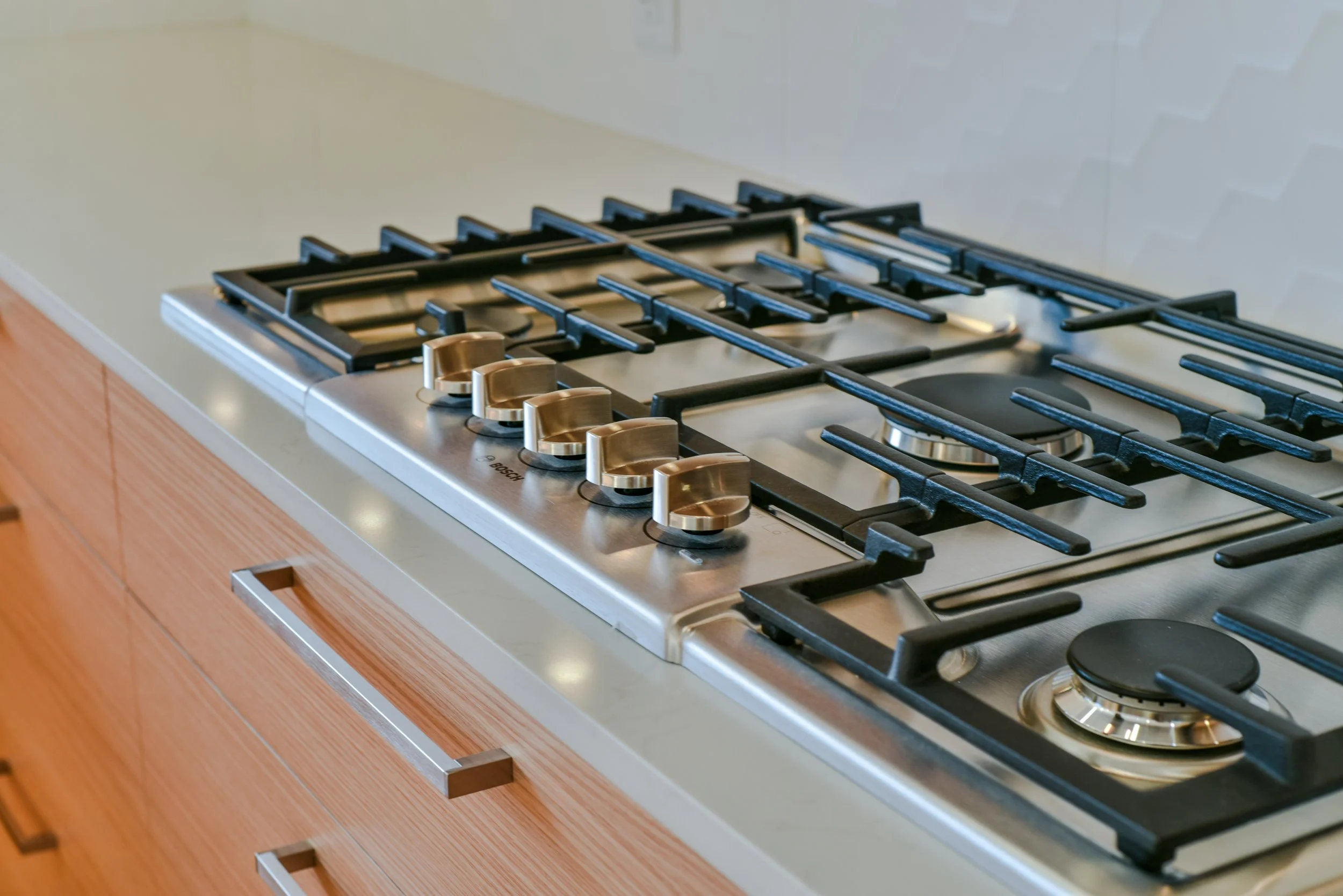 A stainless steel gas stove with five burners on a wooden kitchen countertop.