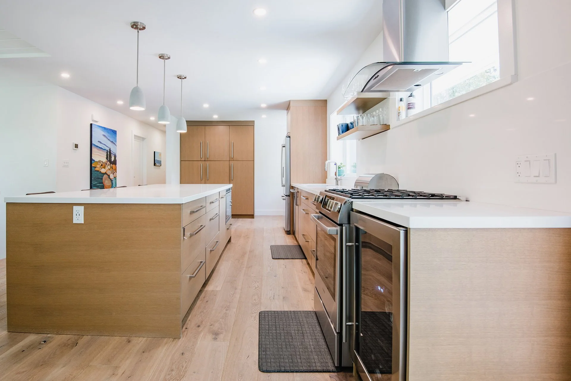 Modern kitchen with wooden cabinets, stainless steel appliances, a large island with white counter, pendant lighting, and hardwood flooring.