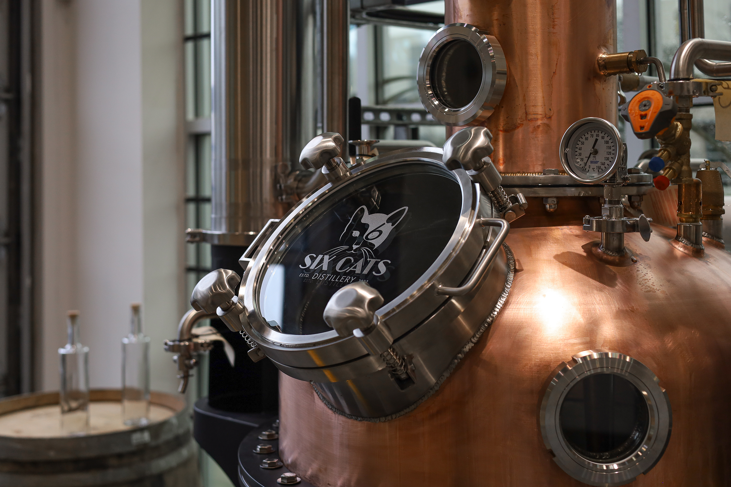 Close-up of a copper distillation apparatus with pressure gauges and metal fittings at a distillery.