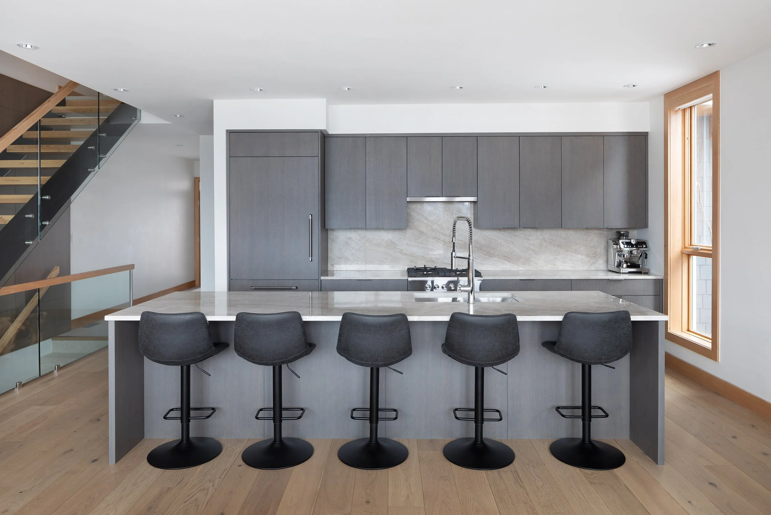 Modern kitchen with gray cabinets, marble backsplash, and an island with black barstools.