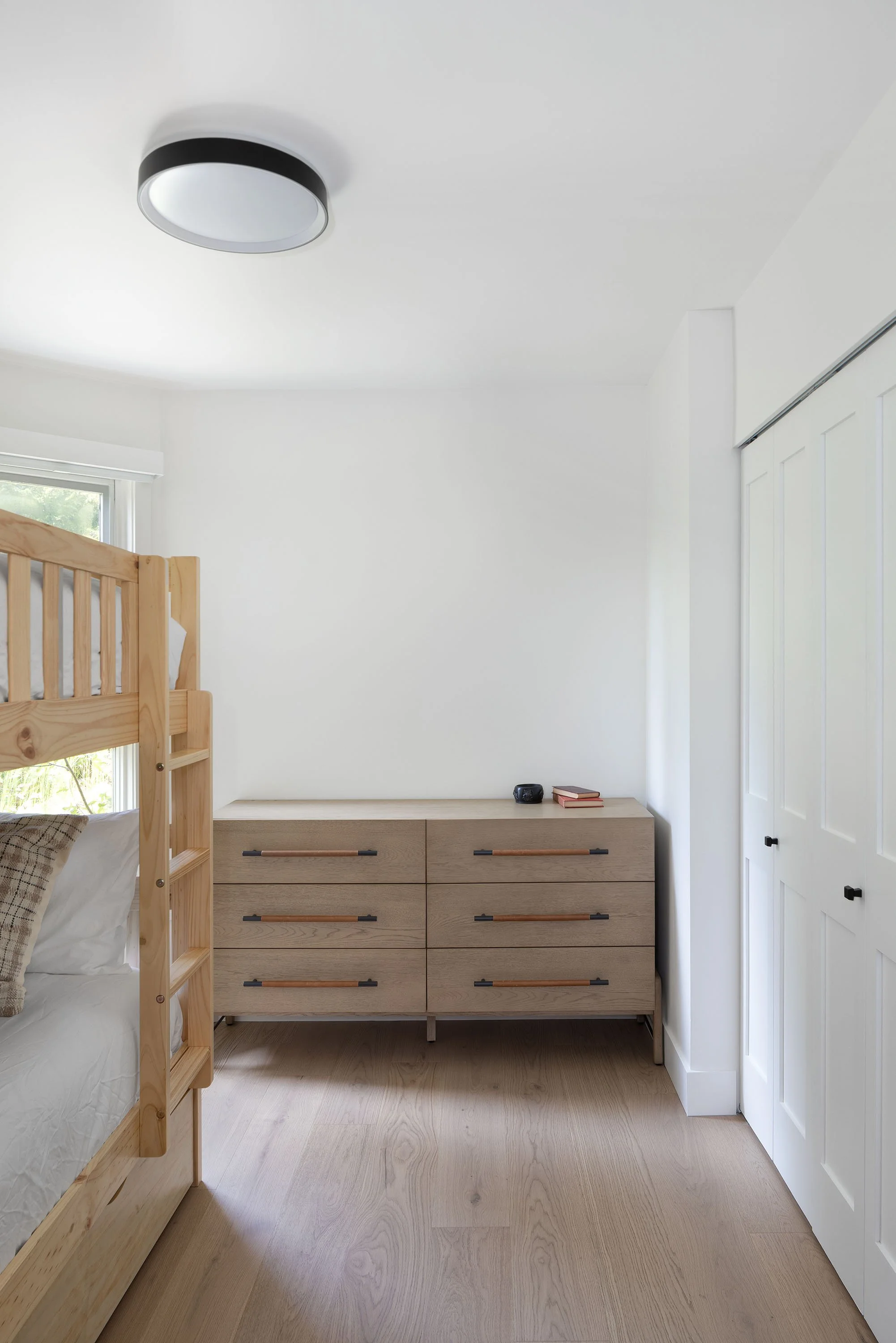 A bedroom with a wooden bunk bed, a dresser, closed white closet doors, and a ceiling light fixture.