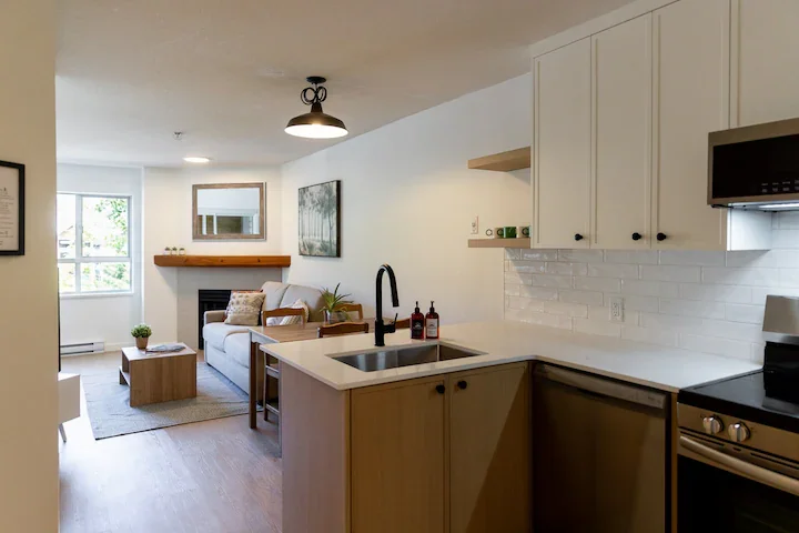 Open-concept living room and kitchen with white walls, natural light, a sofa, coffee table, and wall art.