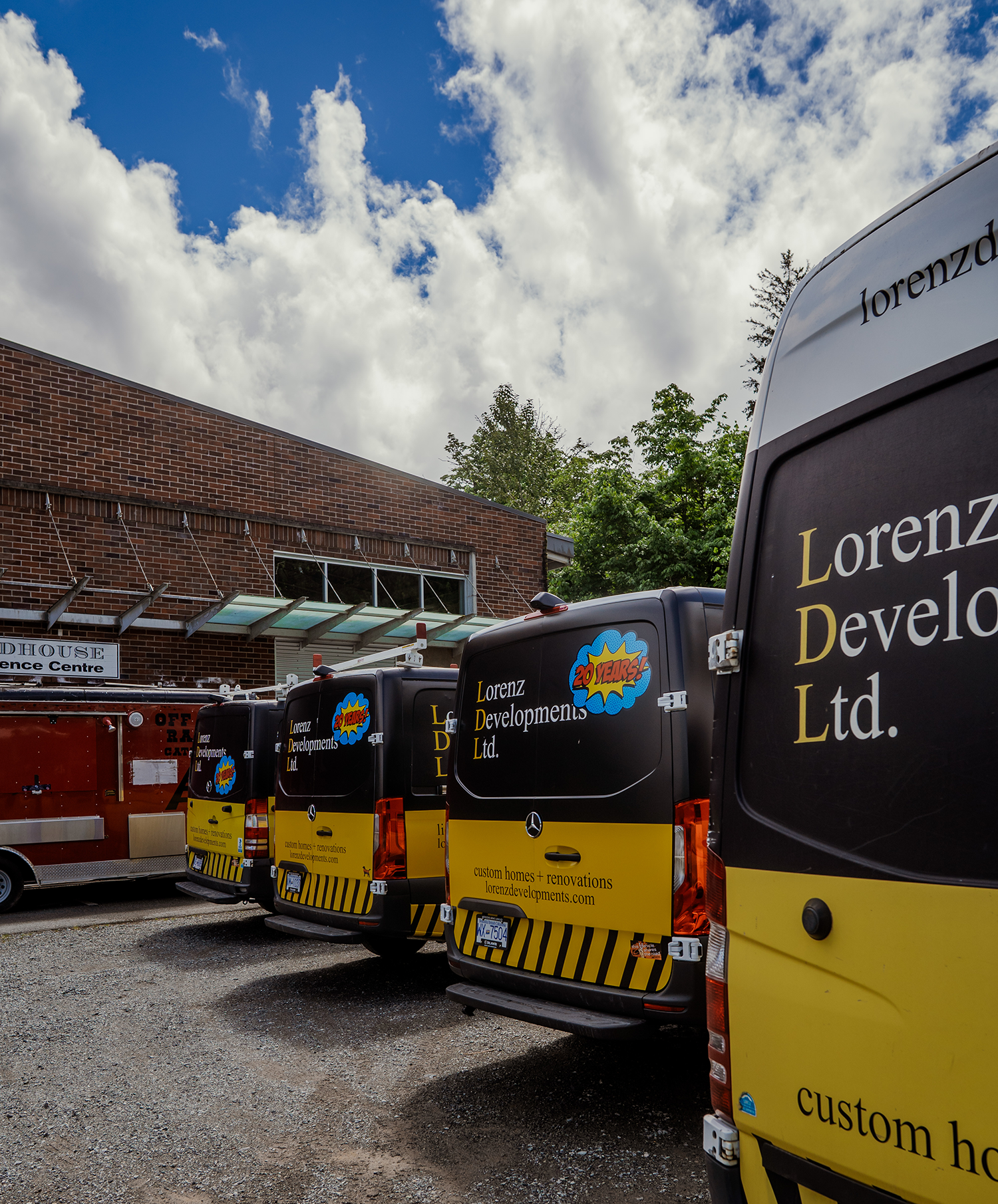 Several black and yellow branded vans parked in front of a brick building under a partly cloudy sky, with some green trees in the background.