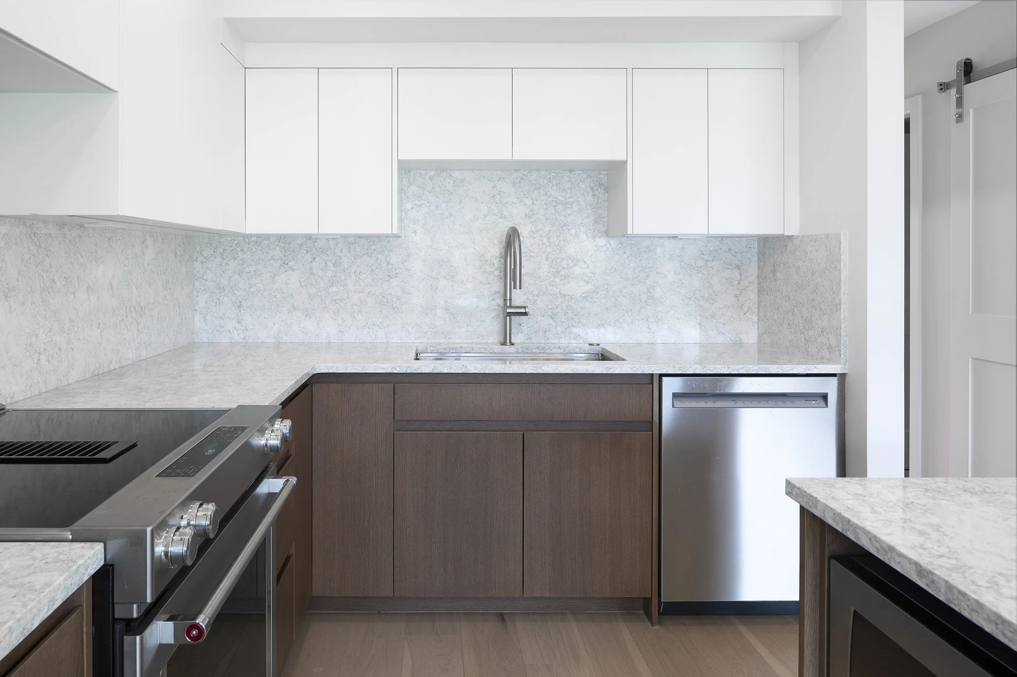 Modern kitchen with white upper cabinets, dark lower cabinets, a marble backsplash, a stainless steel sink and faucet, and a gas stove.