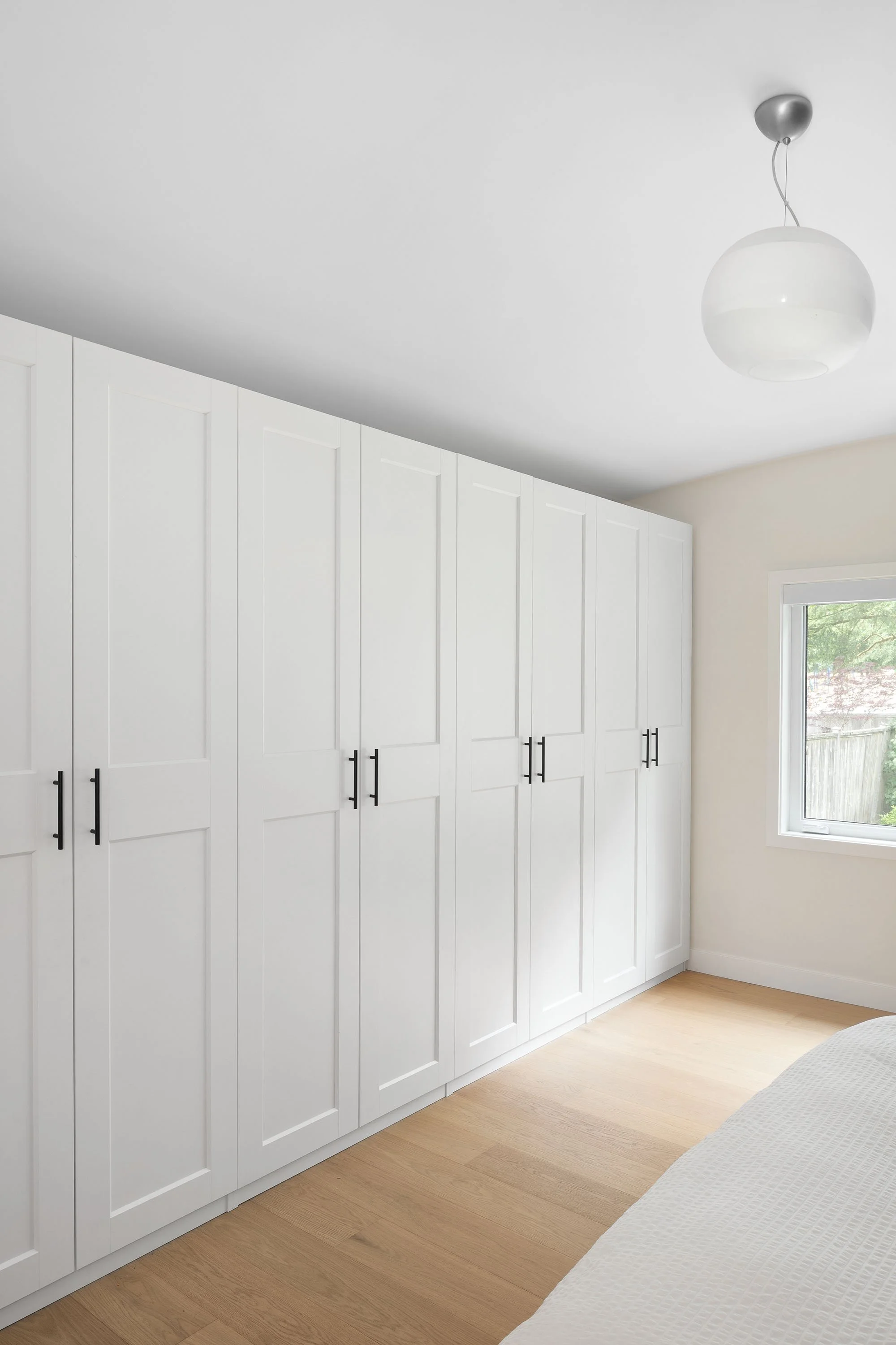 White wardrobe with black handles in a bedroom next to a window and a bed with white textured bedding