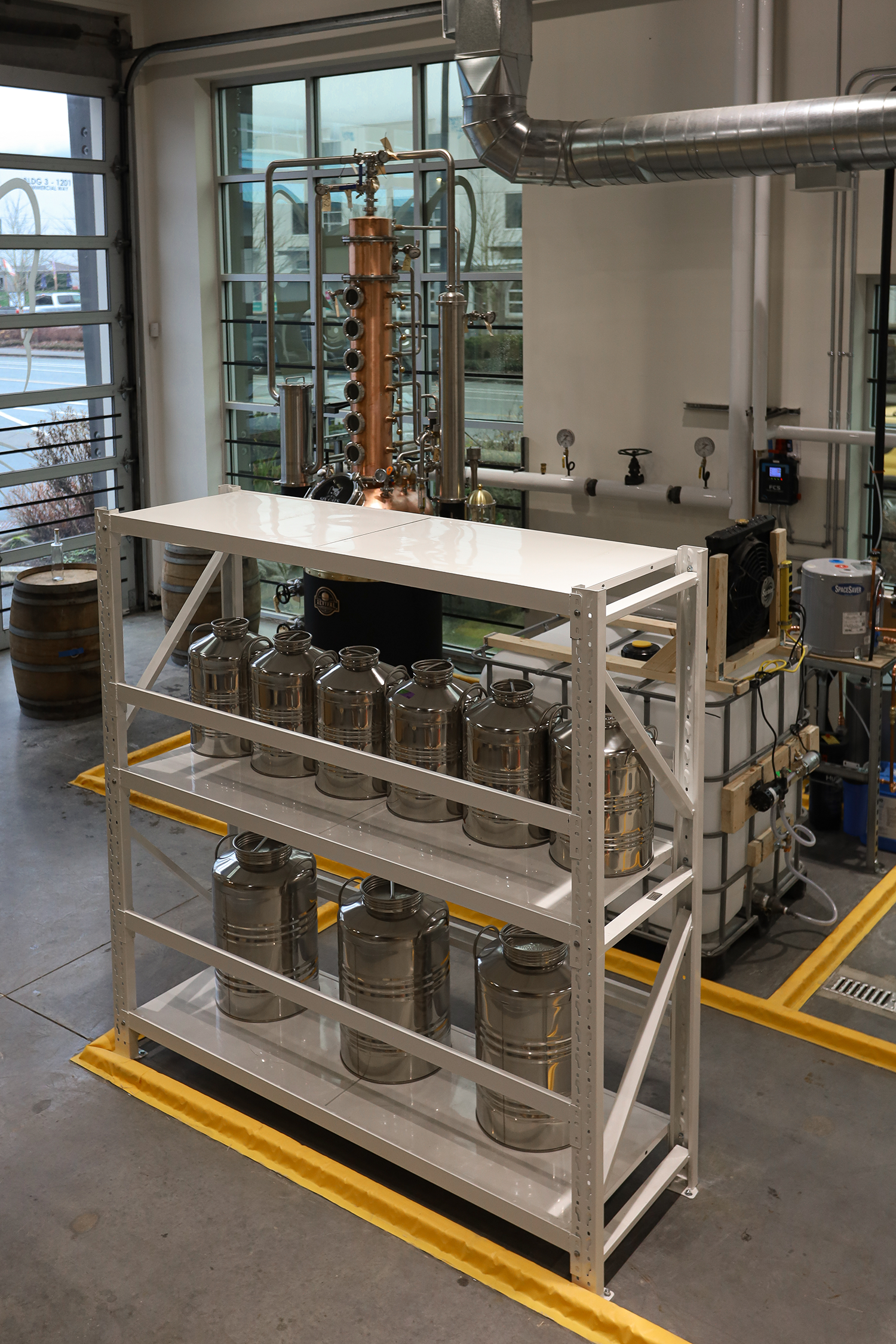 Industrial laboratory setup with a copper distillation column and stainless steel containers on a white metal shelf, located in a bright room with large windows