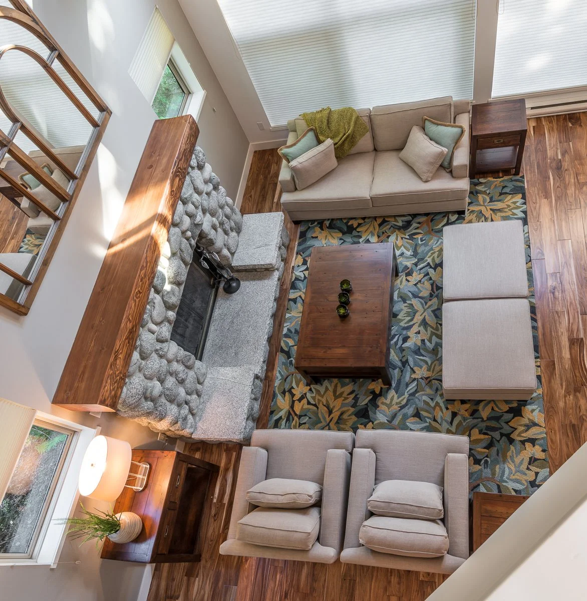 Top-down view of a living room with a fireplace, beige sofa, armchairs, wooden furniture, and a patterned rug.