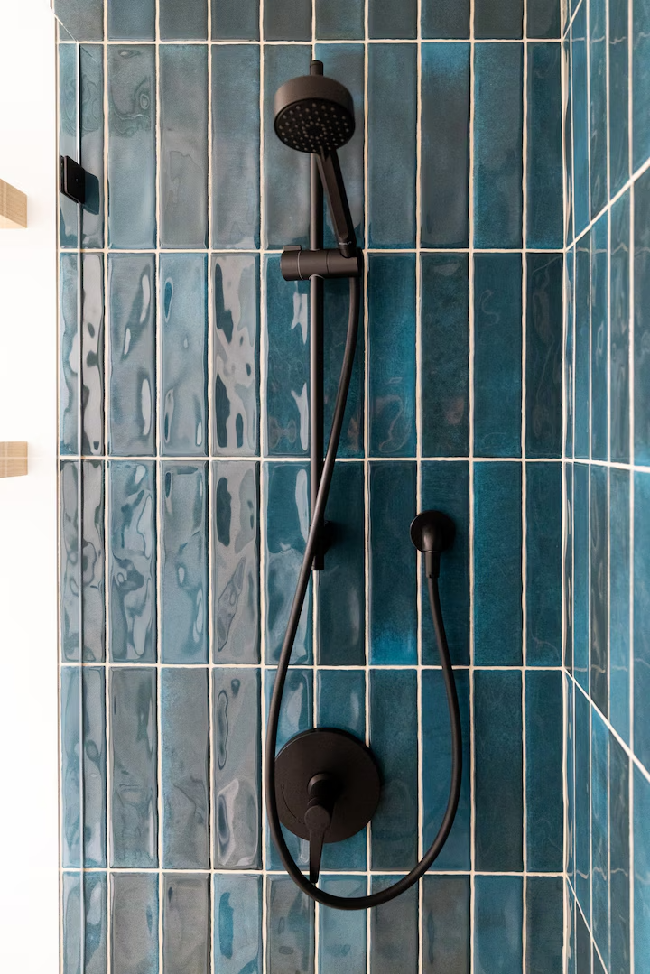 Black showerhead and control panel mounted on a tiled blue bathroom wall.