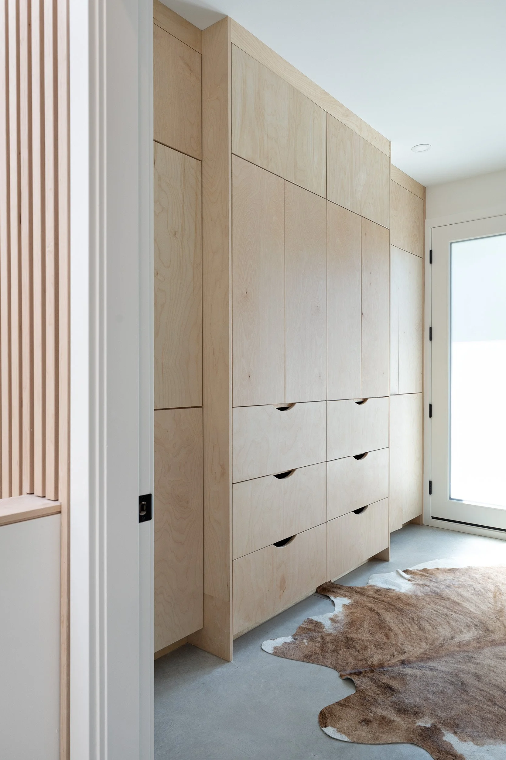 A large wooden cabinet with multiple drawers located near a glass door, with a cowhide rug on the floor in front of it.