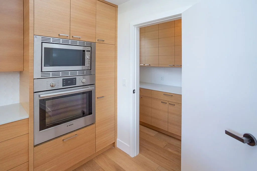Kitchen with light wood cabinets, a built-in microwave and oven, and a doorway leading to another kitchen space with matching cabinets.