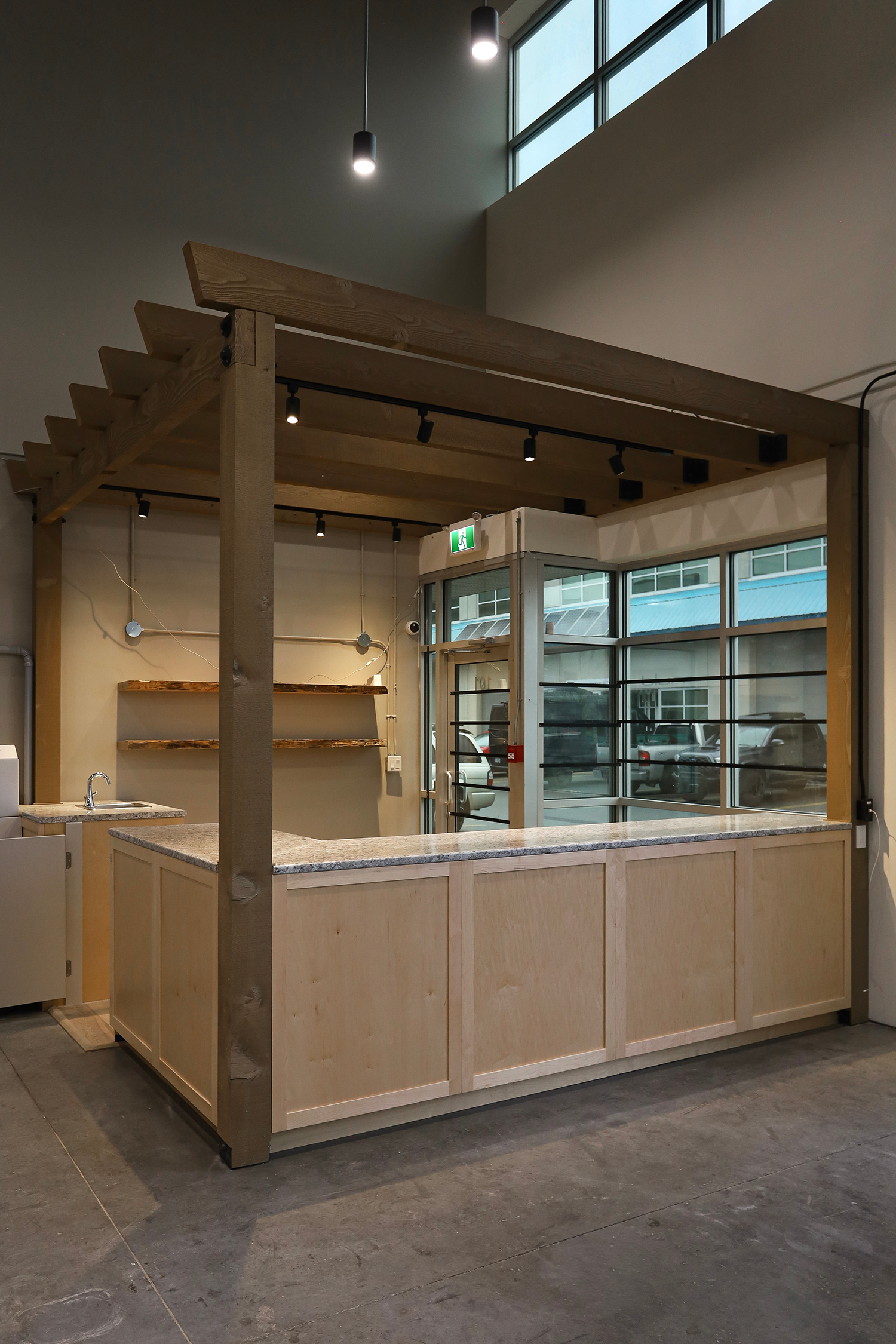 Interior of a modern building with a wooden counter, track lighting, and large glass windows; unfinished workspace with exposed wiring and construction materials.