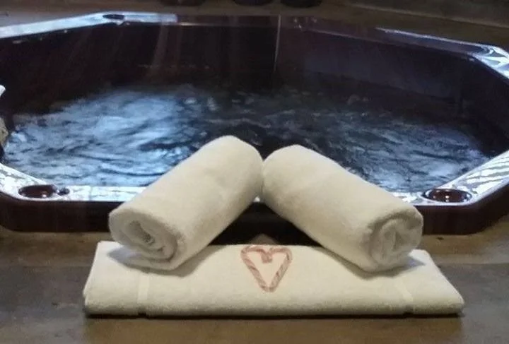 Two rolled-up towels and a towel with a heart design on it placed in front of a hot tub or Jacuzzi.