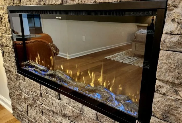 Modern electric fireplace built into a stone wall, with visible flickering flames and logs inside.