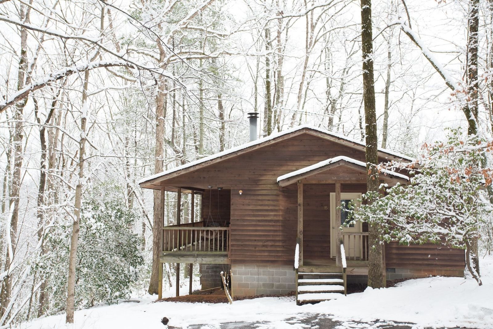 A small wooden cabin in a snowy forest with snow covering the roof and ground.