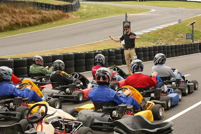 A group of people in go-karts on a race track receiving instructions from a race official or instructor.
