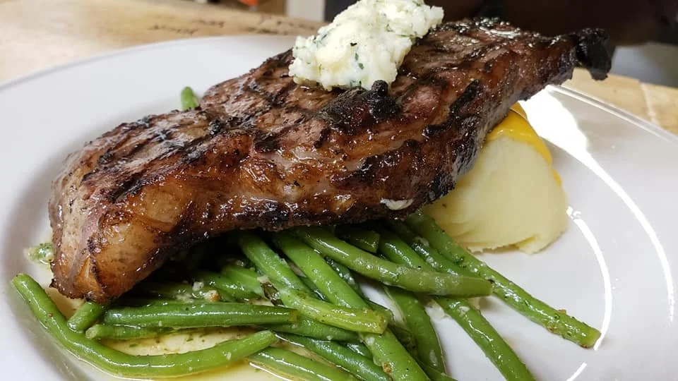 Grilled steak with mashed potatoes, green beans, and a dollop of butter on a white plate.