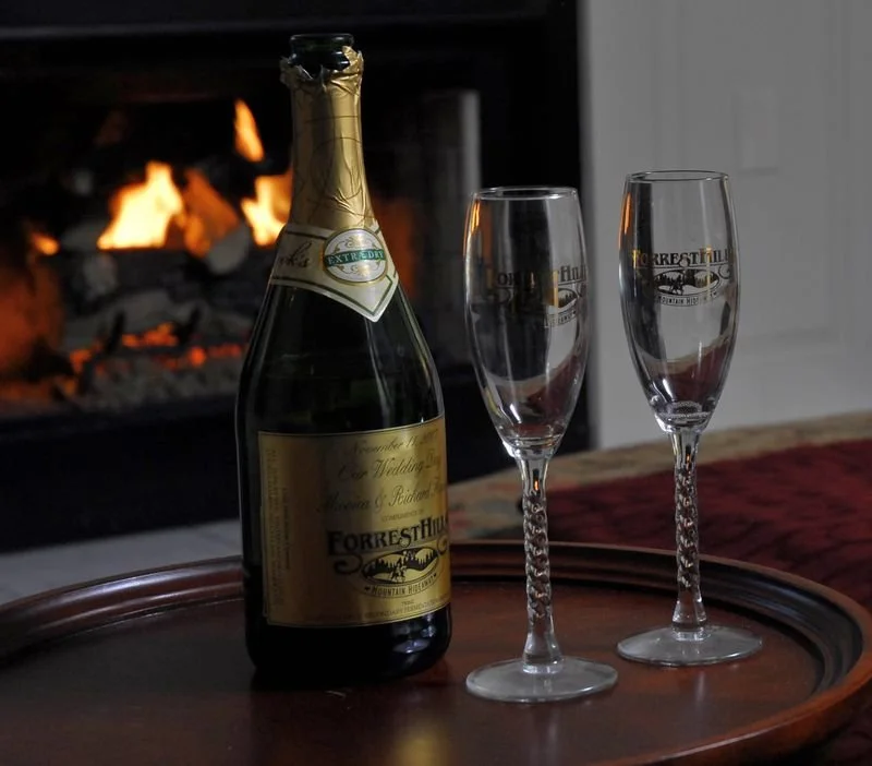 A champagne bottle and two flutes on a tray in front of a fireplace.
