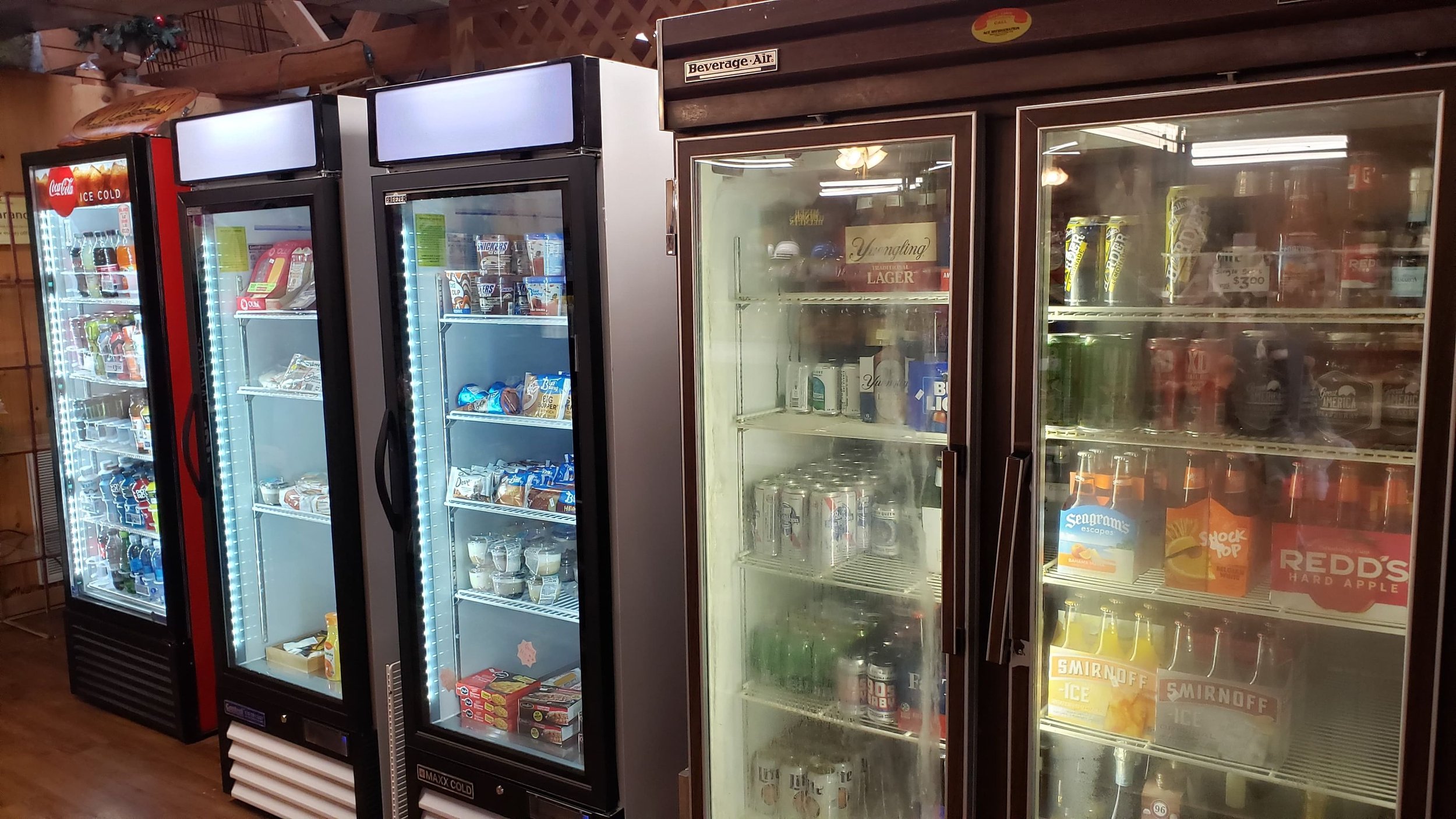 Multiple commercial refrigerators filled with various beverages and snacks in a store aisle.
