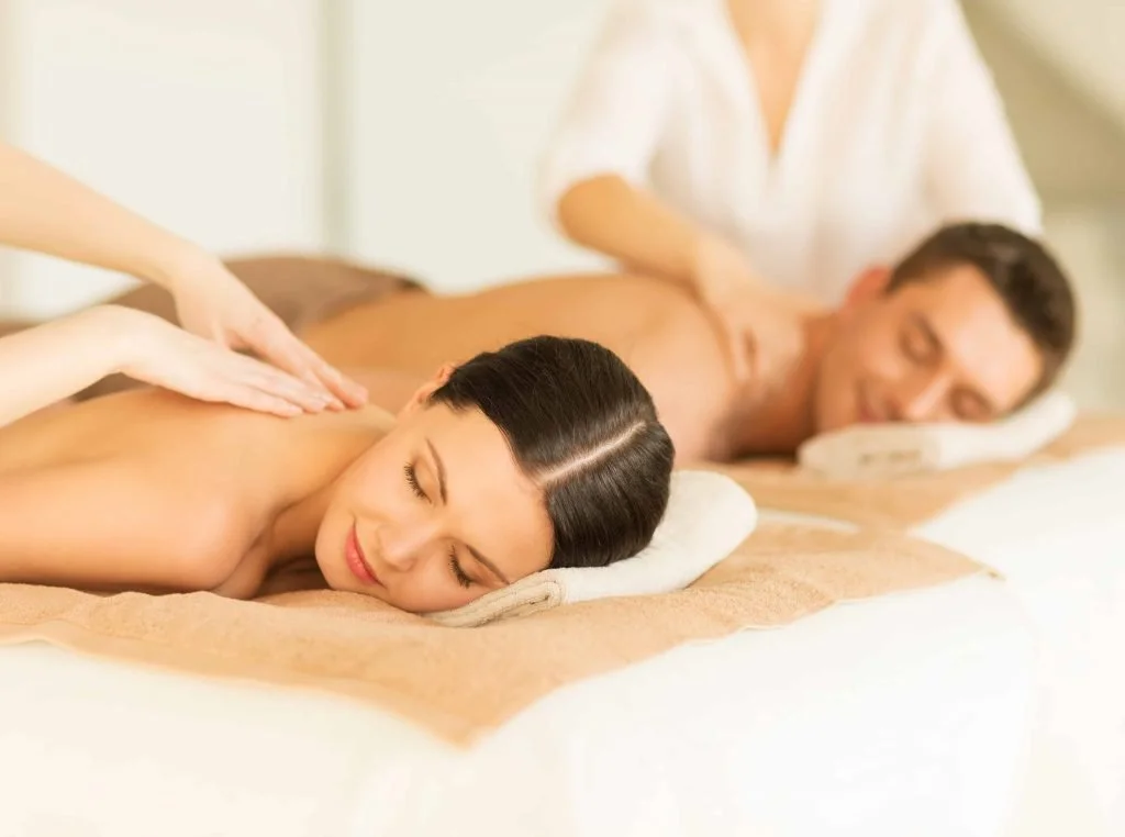 A woman receiving a back massage at a spa with a man lying face down nearby.