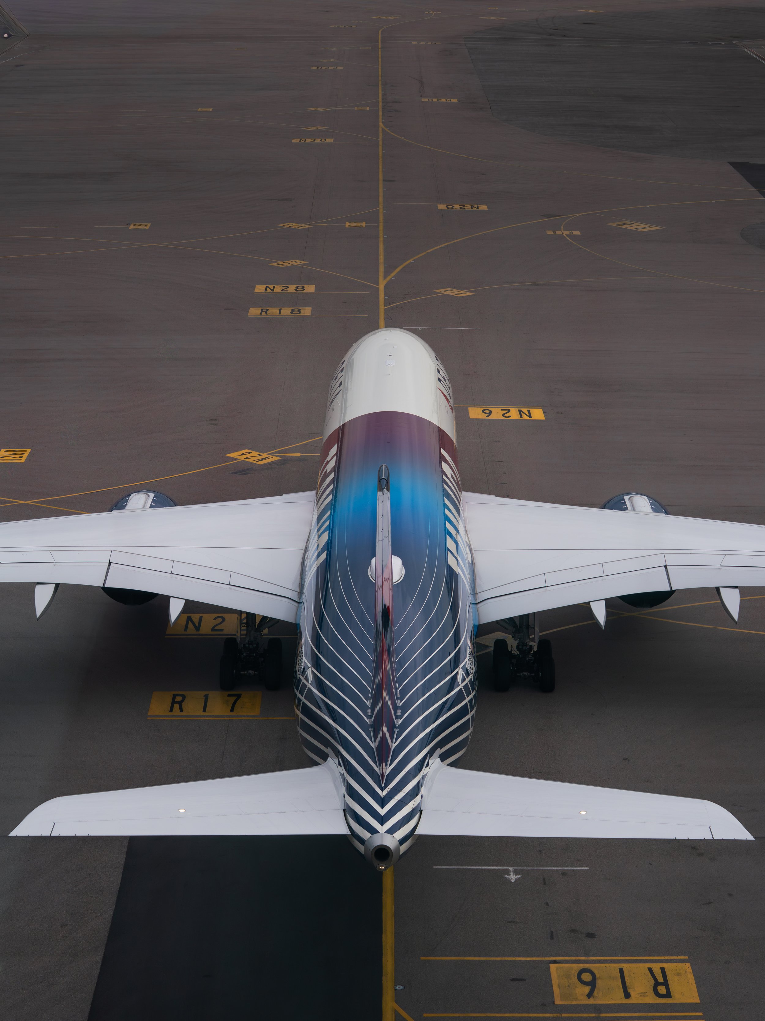 An airplane parked at the gate viewed from above, positioned on the tarmac with various yellow markings and labels nearby.