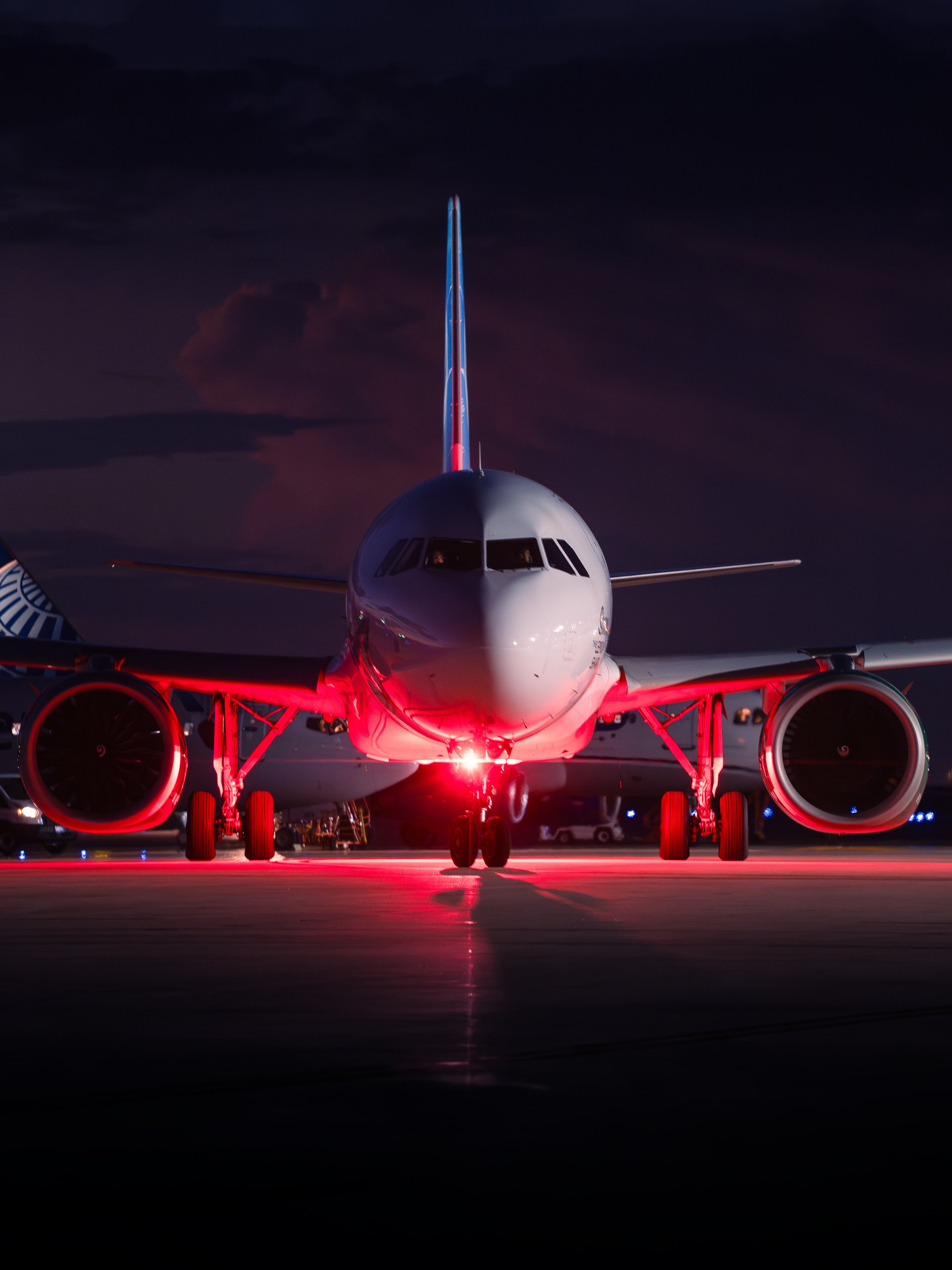 Front view of a commercial airplane parked on the tarmac at night, illuminated by red and white lights.