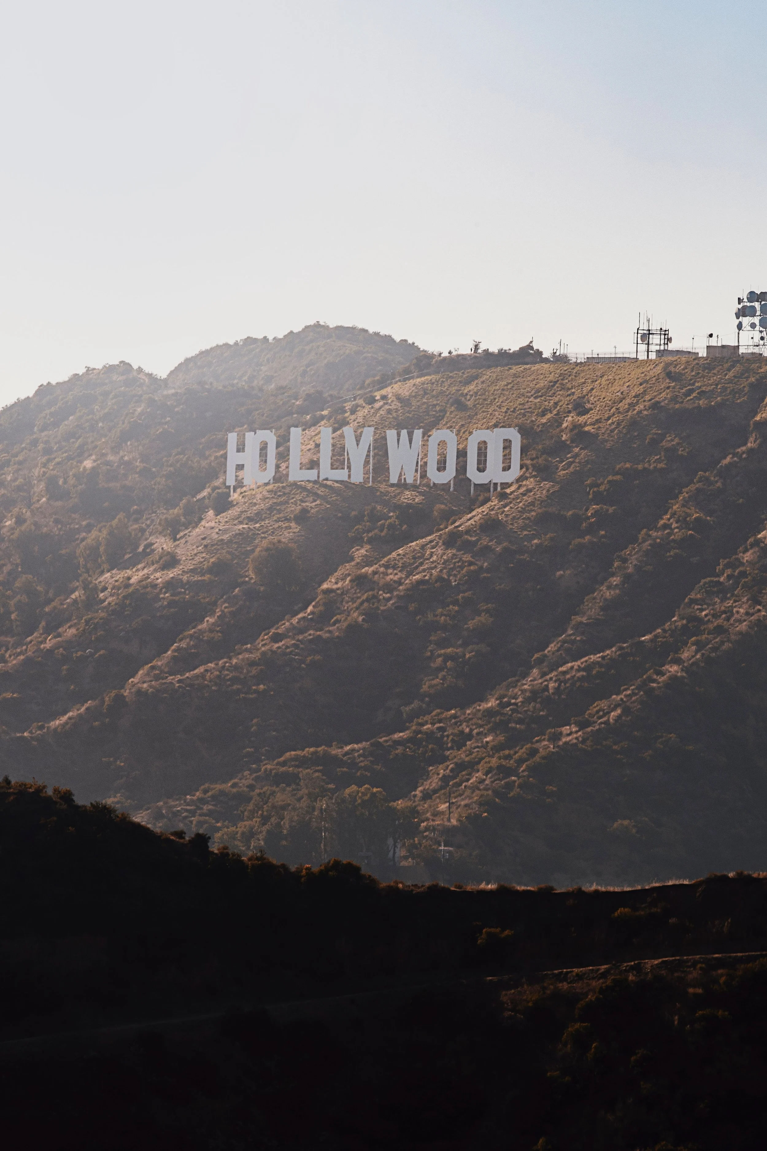 The Hollywood sign on a hillside with some radio and communication antennas on the top, under a clear sky.