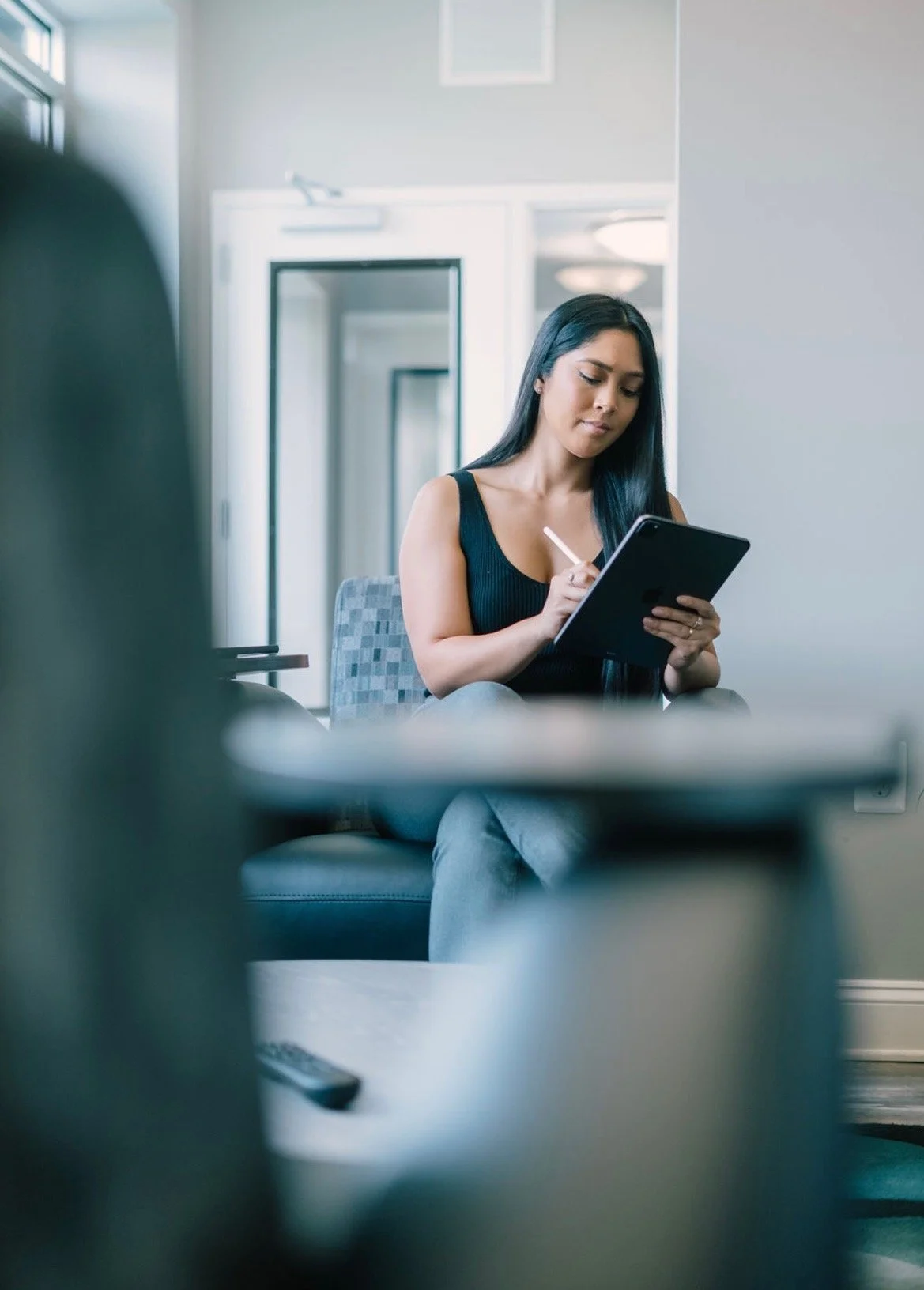 Woman sitting on a chair writing on a digital tablet in a modern, well-lit living room.