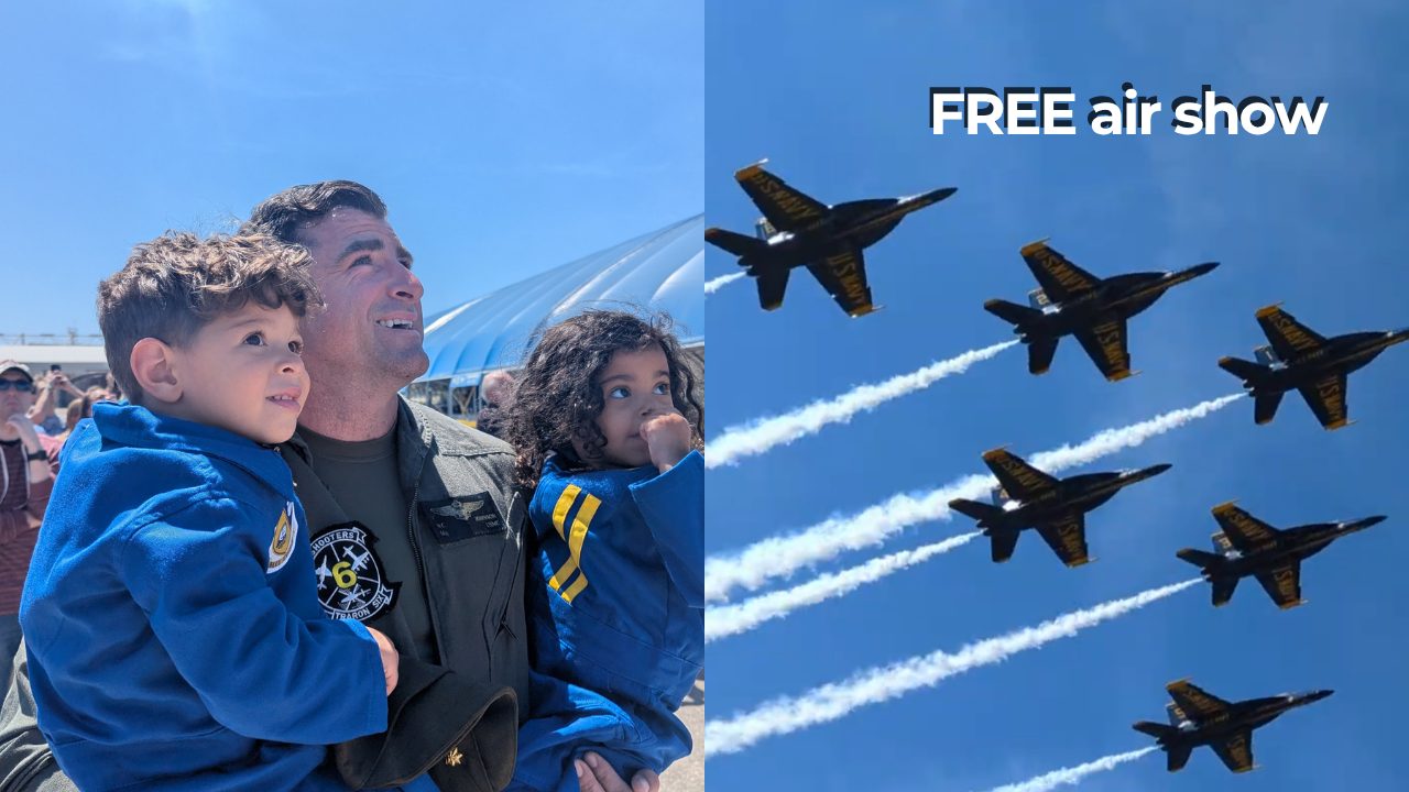 A father in a military flight suit holding his two young children, watching the Blue Angels' practice air show with jets flying overhead in formation, leaving white smoke trails, with a blue sky background at the National Naval Aviation Museum.