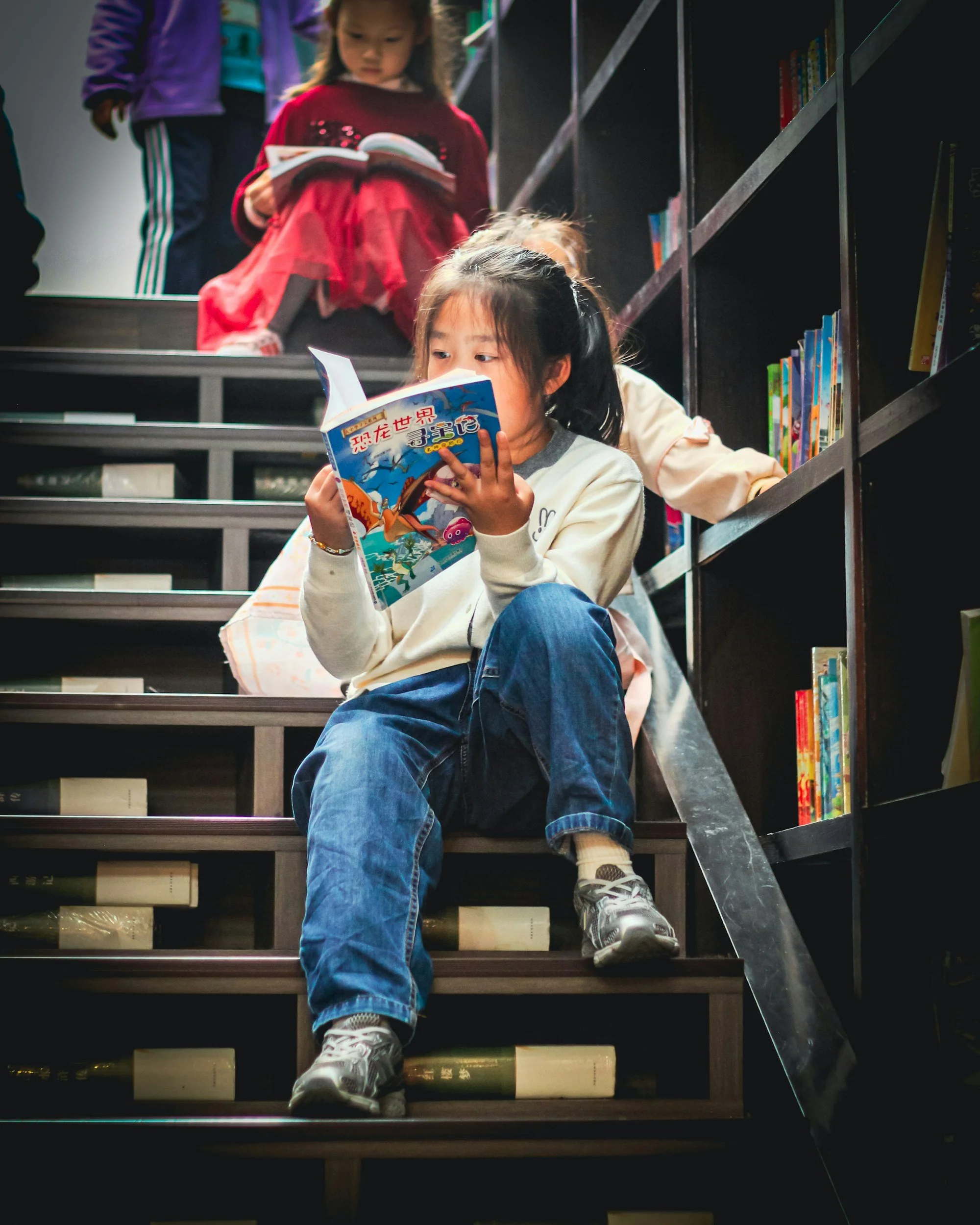 Children reading books on a stairway in a library.