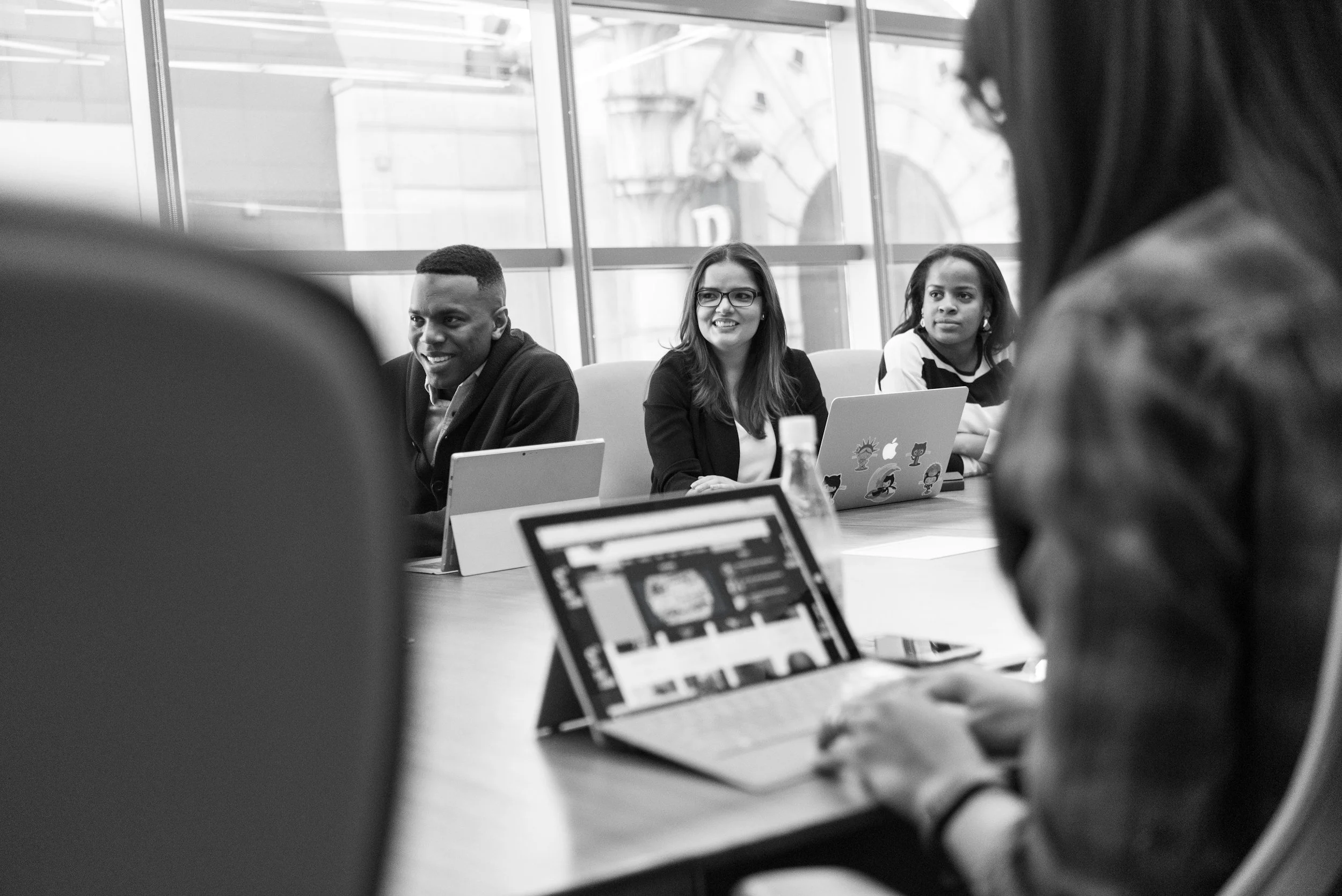 People sitting at a conference table with laptops in a modern office, engaging in discussion.