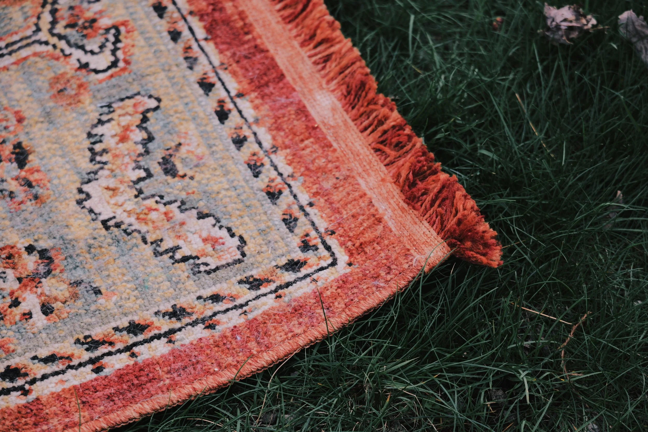 Close-up of an ornate, multicolored rug with fringes, laying on green grass outdoors.
